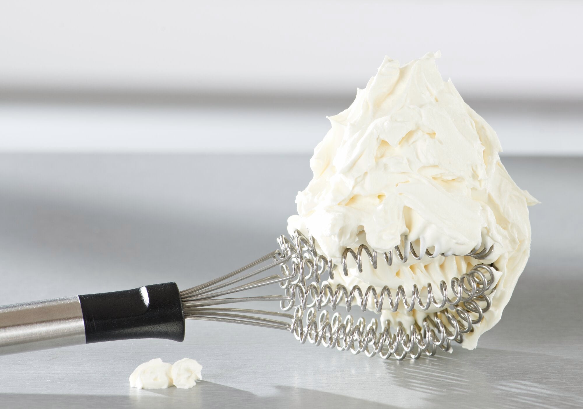 Un fouet appelé Speed Quirl S repose sur une surface lisse. Le fouet est recouvert d'une grande quantité de crème fouettée qui enveloppe ses spirales.