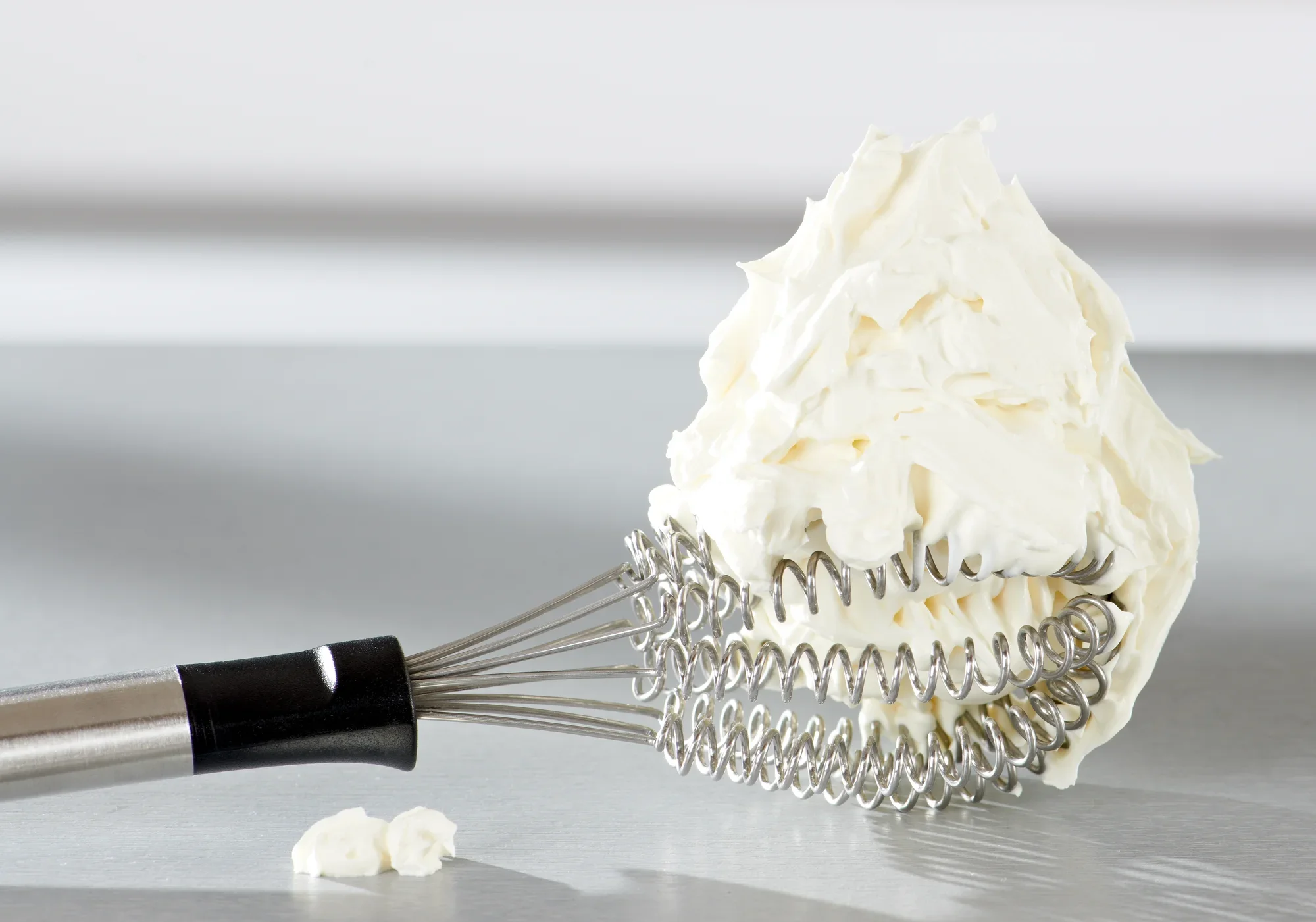 Un fouet appelé Speed Quirl S repose sur une surface lisse. Le fouet est recouvert d'une grande quantité de crème fouettée qui enveloppe ses spirales.