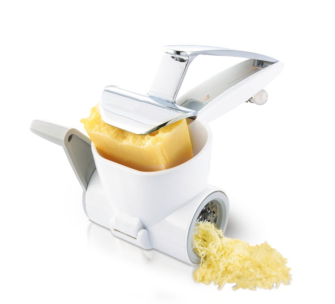 Un rape a fromage blanc avec une poignee grise rape un bloc de fromage jaune, produisant de fines lamelles sur une surface blanche.