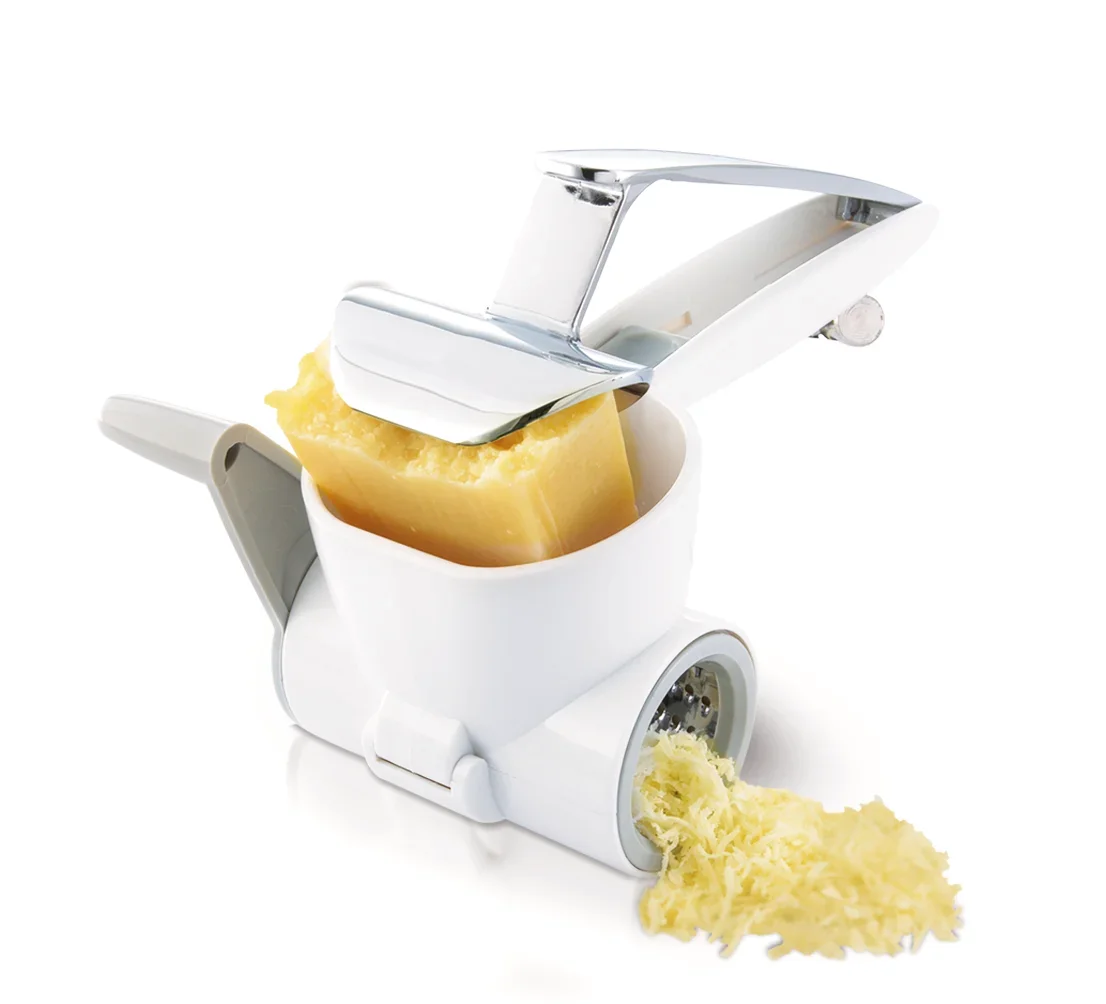 Moulin à fromage en action : un moulin à fromage manuel blanc râpe un gros morceau de fromage. Le fromage fraîchement râpé tombe du moulin sur la surface en dessous. Idéal pour les plats frais.