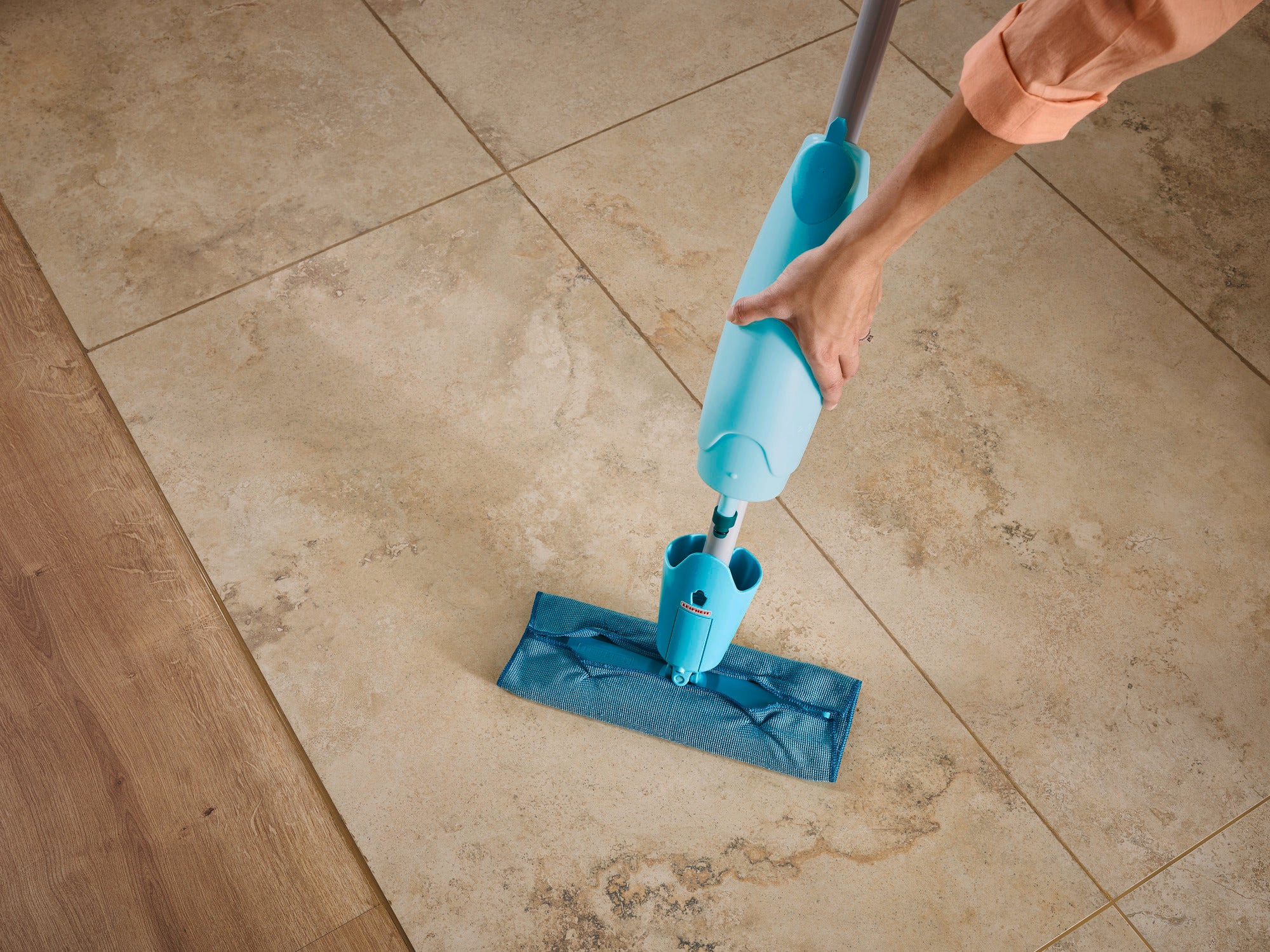 Ein Sprühwischer Pico Spray wird auf einem hellen Fliesenboden verwendet. Der Wischer hat einen blauen Wassertank und ein passendes Wischtuch, das sanft über die Fliesen gleitet.