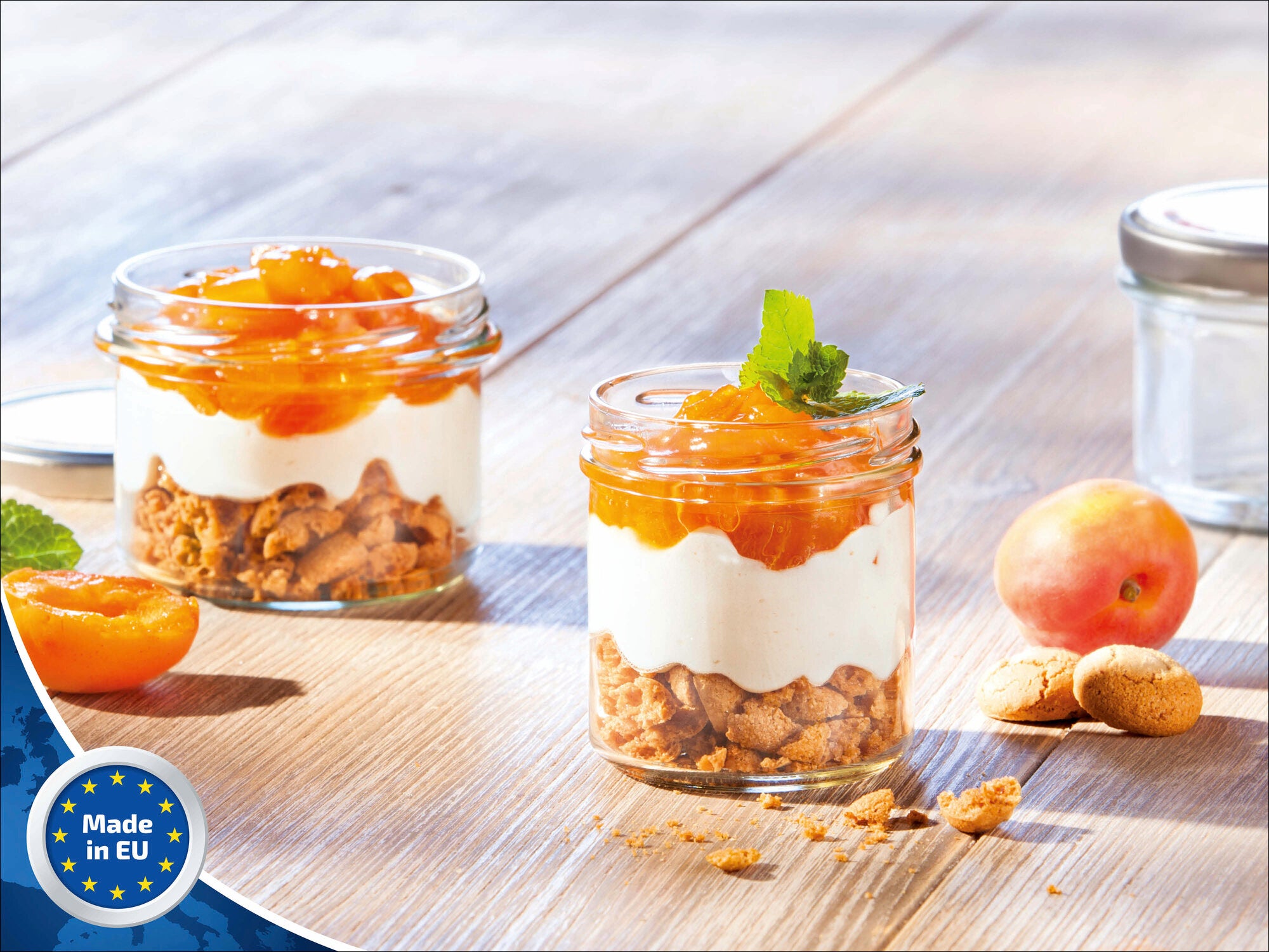 Zwei Leifheit Sturzgläser mit 167 ml Fassungsvermögen, gefüllt mit Schichtdessert aus Keksen, Sahne und Aprikosen, stehen auf einem Holztisch. Ein Glas ist geöffnet, daneben liegen Aprikosen und Kekse.