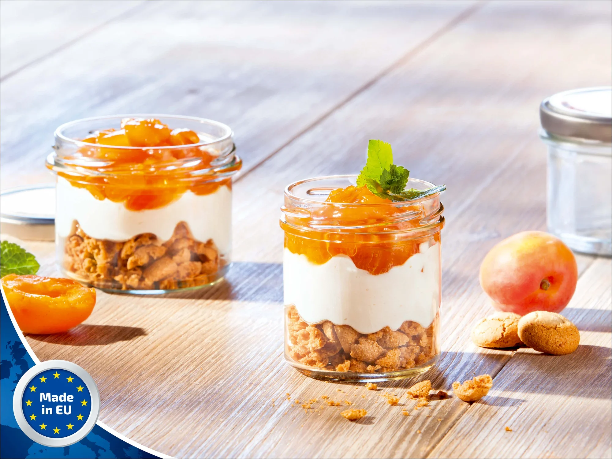 Zwei Leifheit Sturzgläser mit 167 ml Fassungsvermögen, gefüllt mit Schichtdessert aus Keksen, Sahne und Aprikosen, stehen auf einem Holztisch. Ein Glas ist geöffnet, daneben liegen Aprikosen und Kekse.