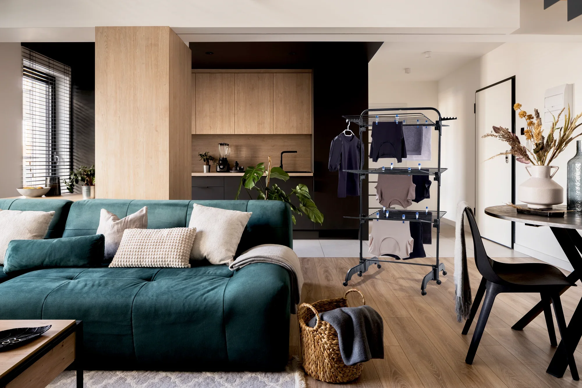 Séchoir à tour Comfort Tower 420 dans un salon moderne. Le séchoir noir est placé à côté d'un canapé vert et d'une table à manger, entouré d'un mobilier élégant.