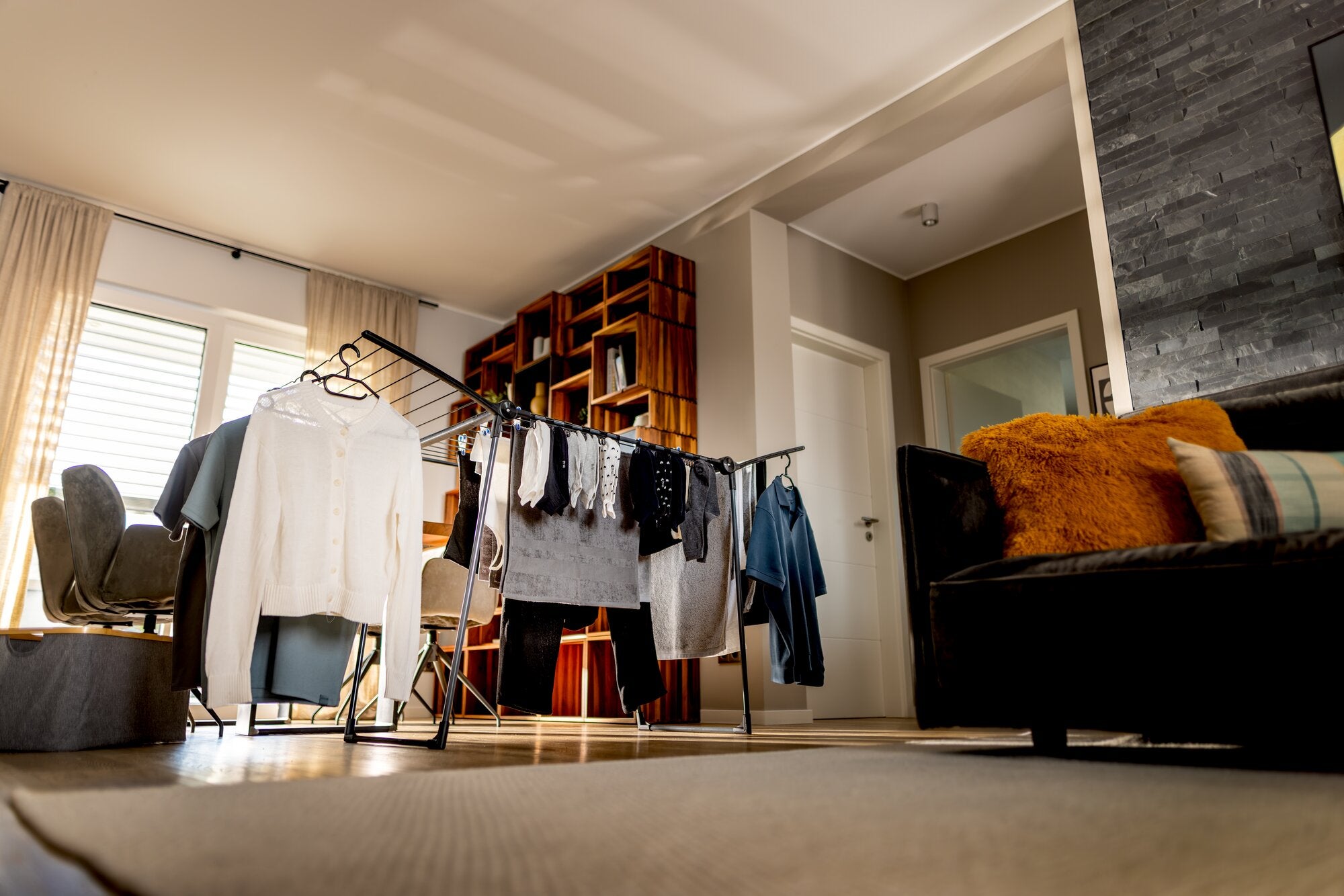 Leifheit Wäscheständer Pegasus Ultra Black 23 m in modernem Wohnraum aufgestellt, mit Hemden, Pullover, Handtüchern und Jeans behängt, neben Sofa und Regal im warmen Tageslicht.