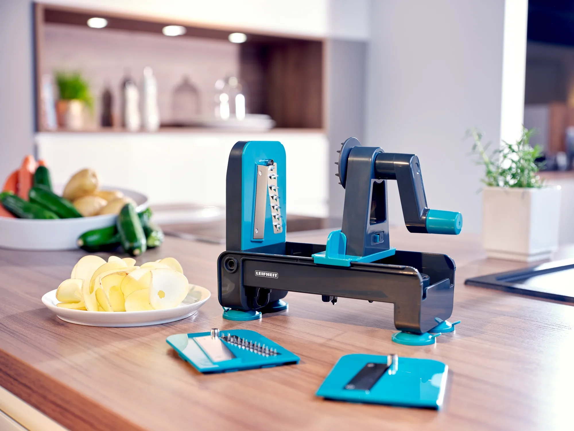 Ein Tisch-Spiralschneider in einer modernen Küche. Der Spiralschneider ist blau und schwarz, mit verschiedenen Klingen und geschnittenen Äpfeln auf einem Teller.