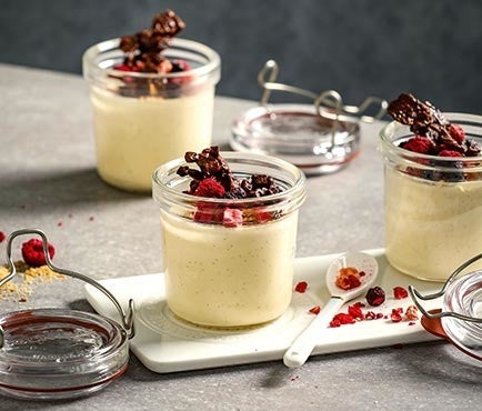 Drei Cheesecakes im Glas auf einem weissen Teller, garniert mit Schokoknusper und Himbeeren.