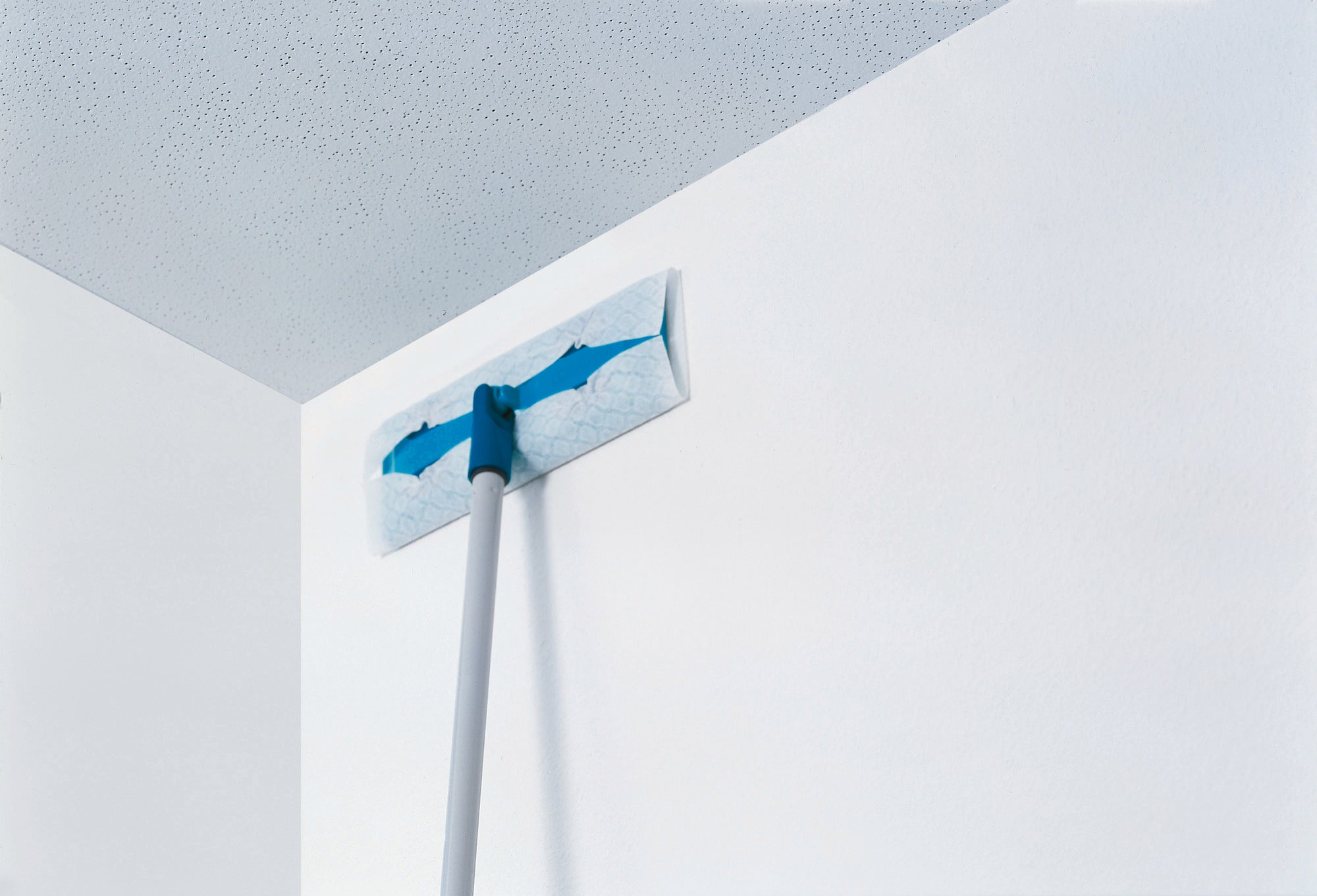 Ein Bodenwischer reinigt eine Fläche. Der Wischer hat einen blauen Einsatz und einen langen Stiel, ideal für schwer erreichbare Stellen.