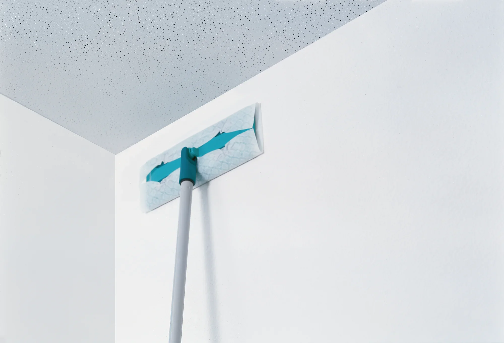 Una mopa limpia una superficie. La mopa tiene un inserto azul y un mango largo, ideal para lugares de difícil acceso.