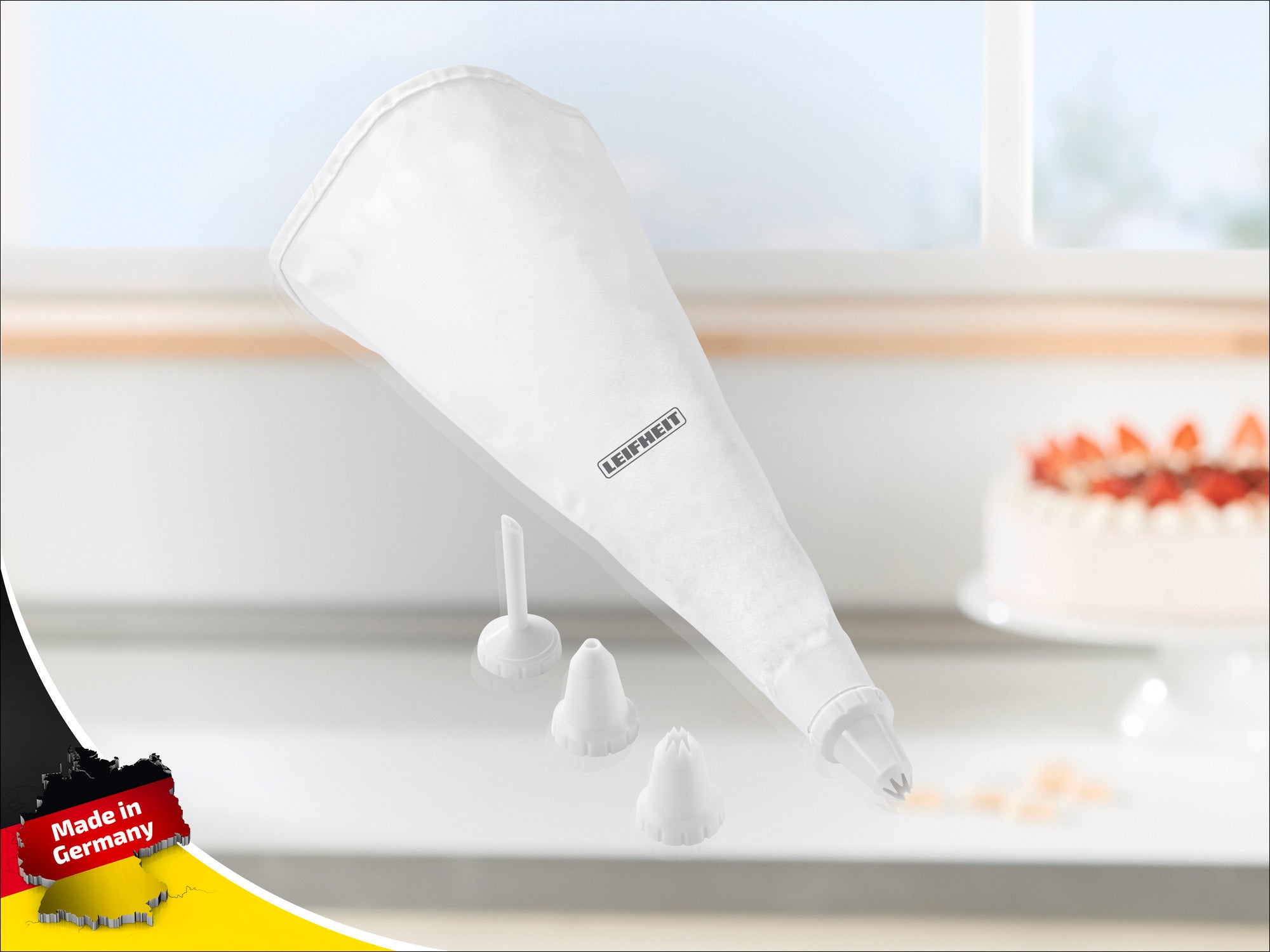 A piping bag from Leifheit with three different nozzles lies on a kitchen worktop. A decorated cake can be seen in the background. Made in Germany.
