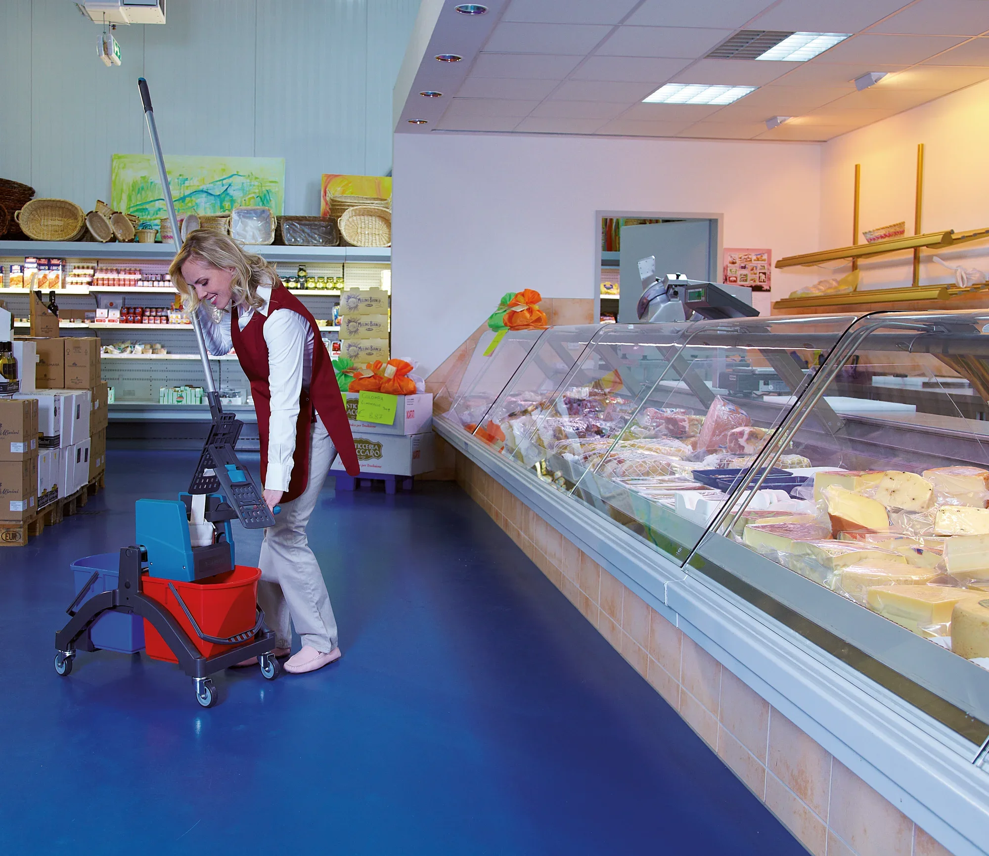 Kobieta myje podłogę w supermarkecie za pomocą wózka do mopowania na mokro Professional Duo. Wózek ma dwa wiadra i długi uchwyt, idealny do wydajnego mopowania.