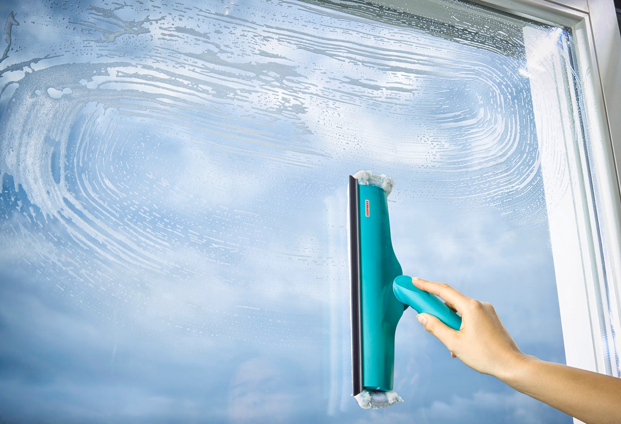 Ein Fensterwischer 3in1 wird verwendet, um ein großes Fenster zu reinigen. Die Hand hält den ergonomischen Griff, während das Fenster klar und streifenfrei wird. Ideal für eine gründliche Reinigung.