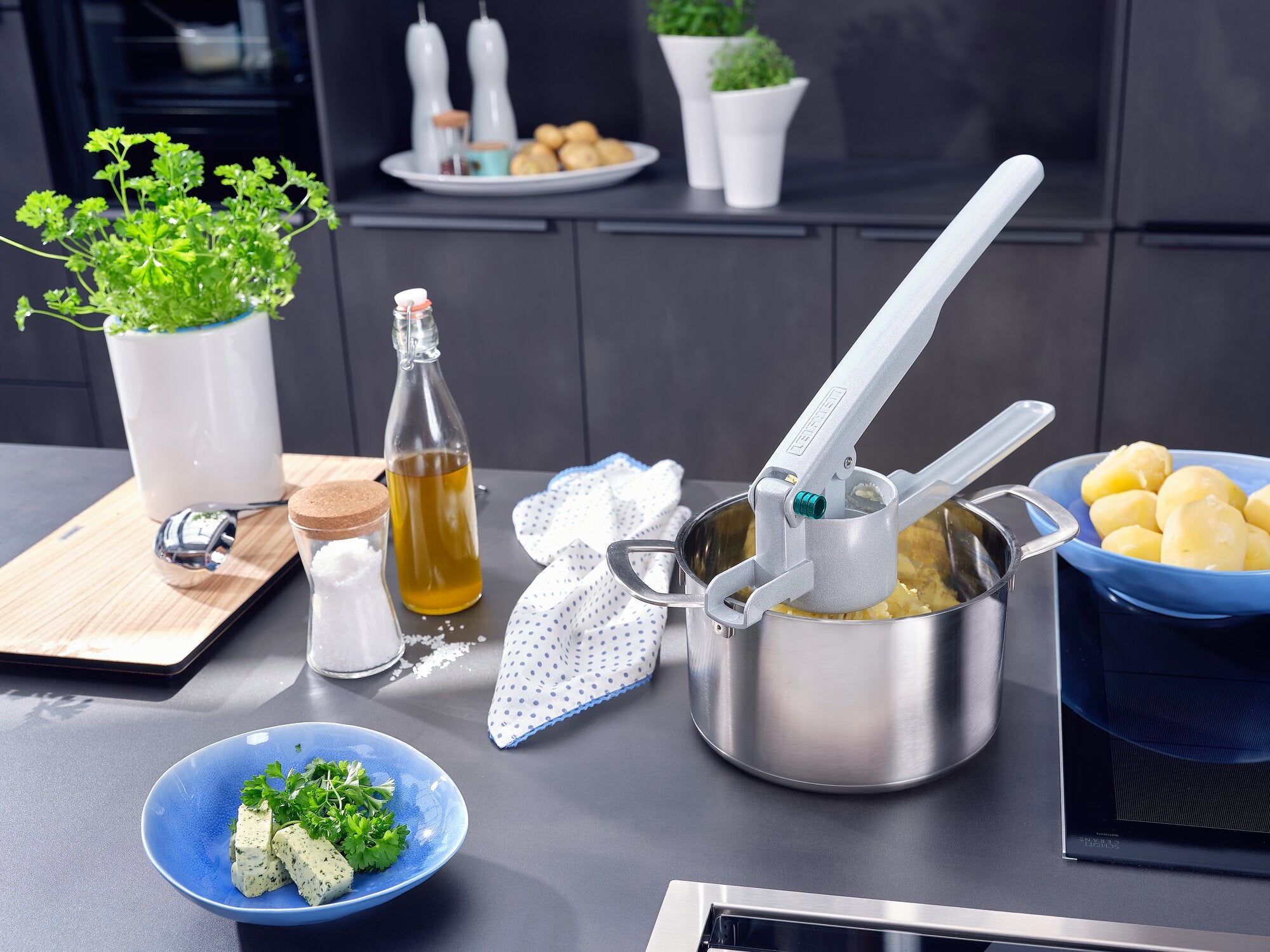 Aardappelpureetpers in een moderne keuken. De ricer wordt boven een pot geplaatst om aardappelen te persen. Verse kruiden en specerijen staan op tafel.