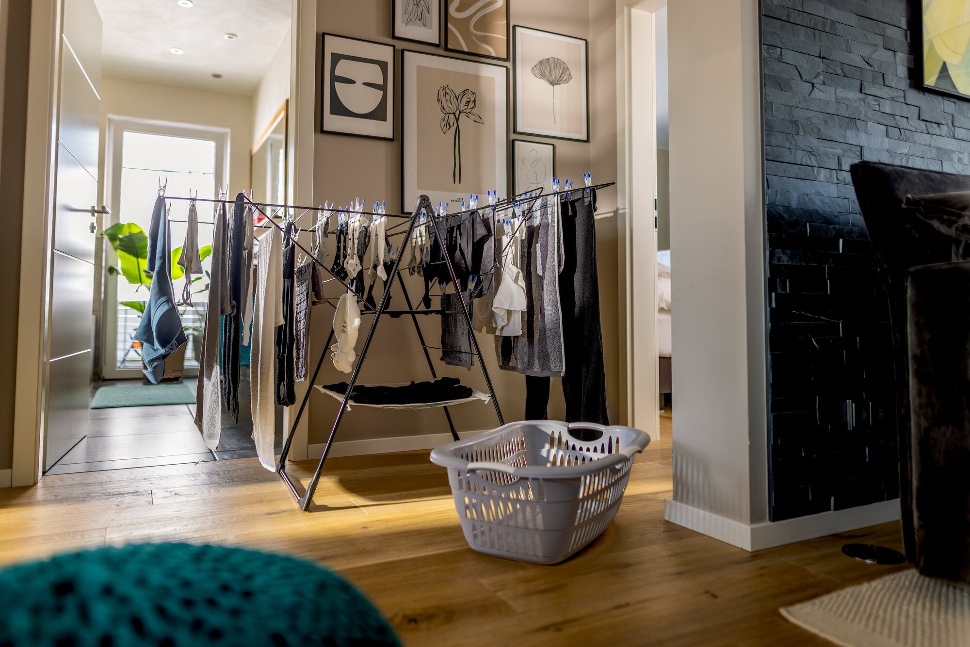 Leifheit Wäscheständer Classic 250 Flex Black in Schwarz, aufgestellt im Flur einer Wohnung und mit vielfältiger Wäsche behängt; daneben steht ein grauer Wäschekorb auf hellem Holzboden.