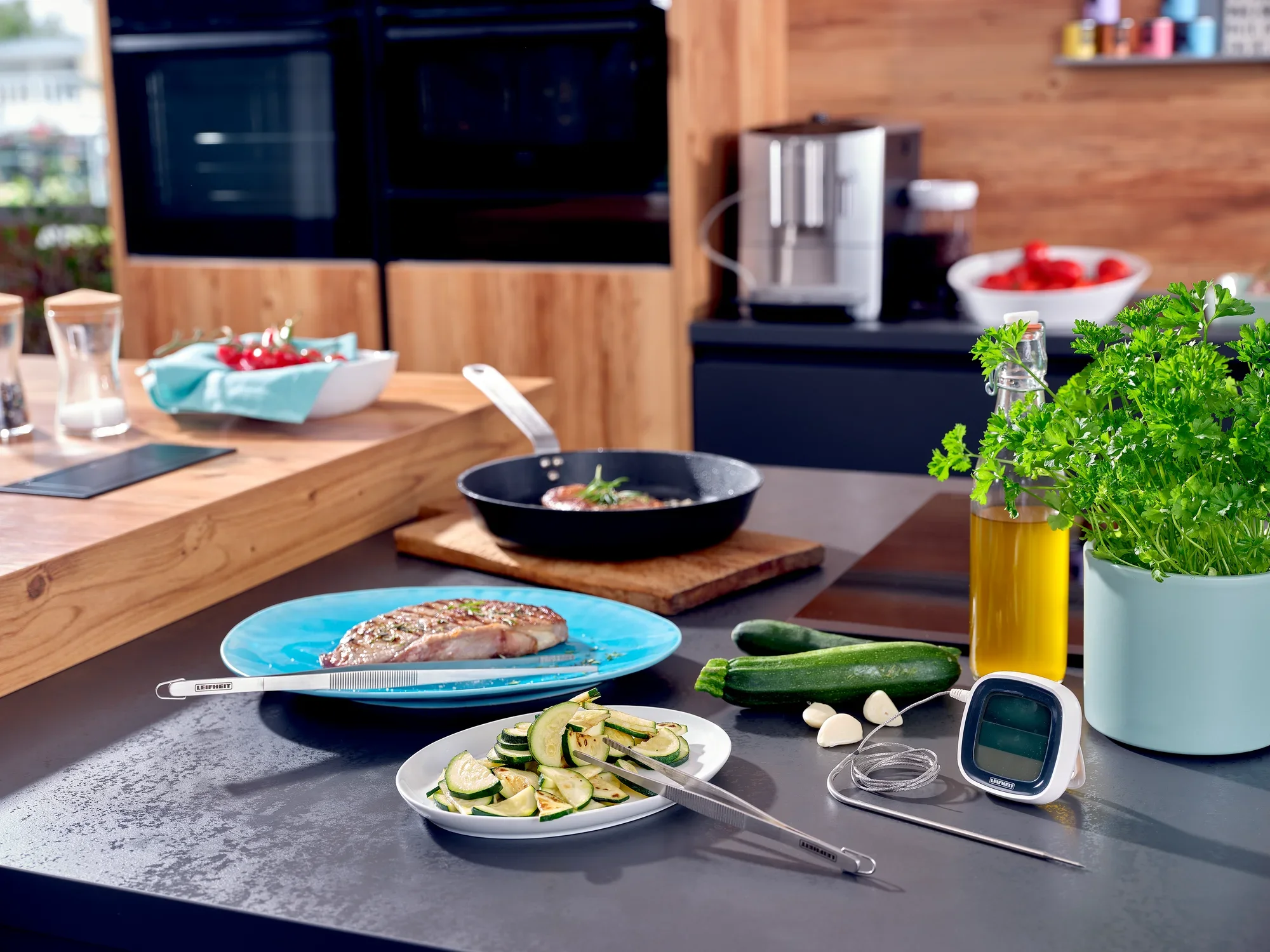 W nowoczesnej kuchni pęseta kuchenna o długości 30 cm leży obok talerza z grillowaną rybą i plastrami cukinii. Widoczne są również świeże zioła i oliwa z oliwek.