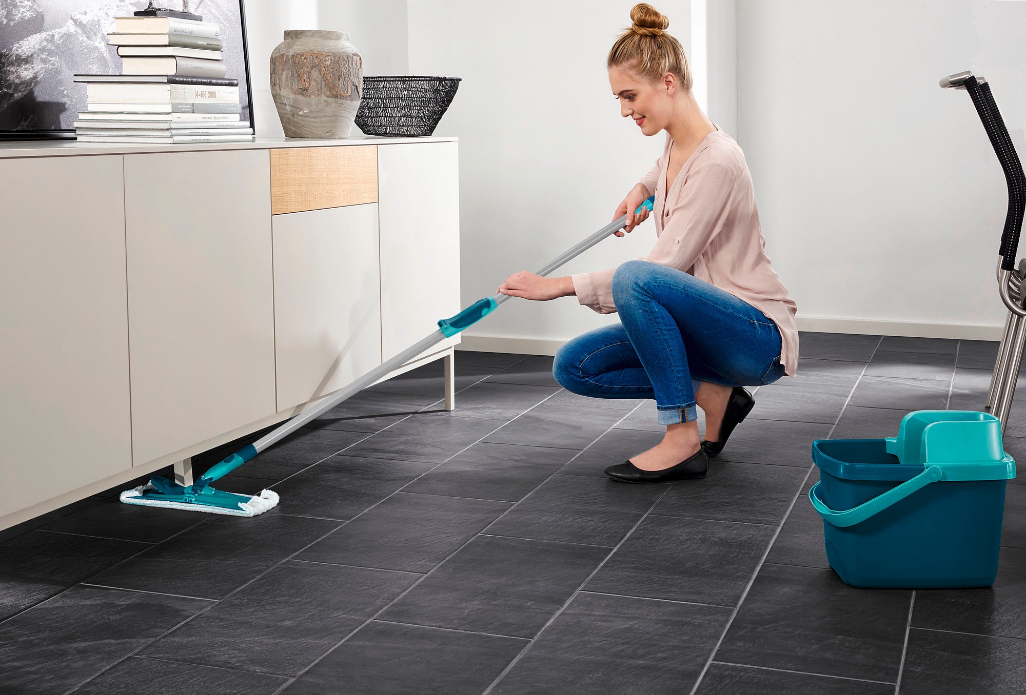 Eine Frau reinigt den Boden mit dem Bodenwischer Combi M micro duo mit Teleskopstiel. Der Wischer erreicht mühelos schwer zugängliche Stellen unter Möbeln. Ideal für eine gründliche Reinigung.