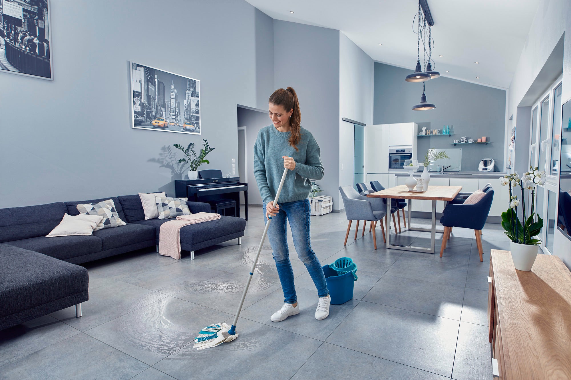 Una mujer limpia el suelo de un salón moderno con la Power Mop 3in1. La habitación es luminosa y está decorada con estilo, con un gran sofá y una mesa de comedor al fondo.