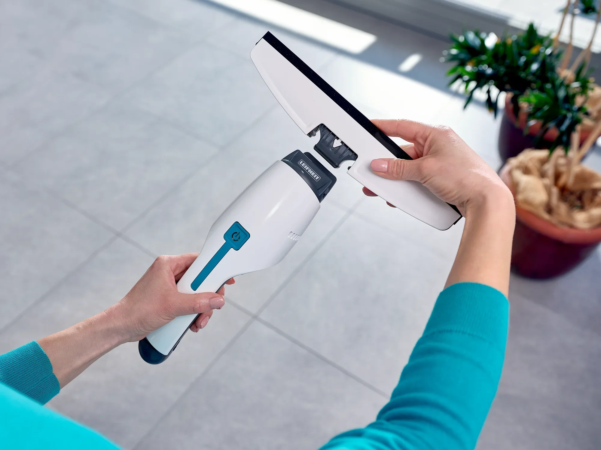 Une personne nettoie une fenêtre avec l'aspirateur pour vitres Nemo. L'aspirateur a un design ergonomique et une surface blanche avec des accents bleus. Idéal pour une propreté sans traces.