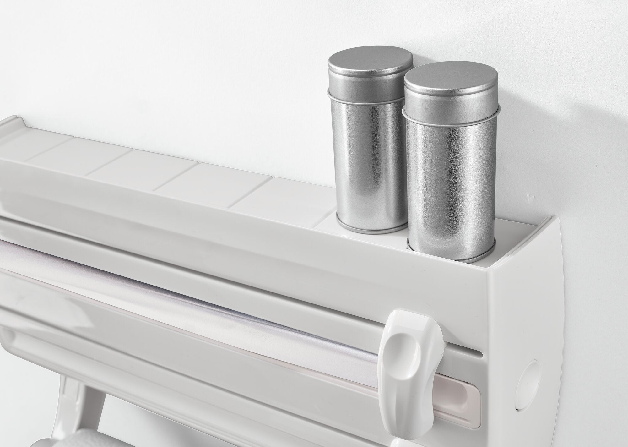 Parat F2 wall-mounted roll holder in white, mounted on a wall. Two silver tins stand on top of the holder. Ideal for the kitchen or workshop for storing rolls.