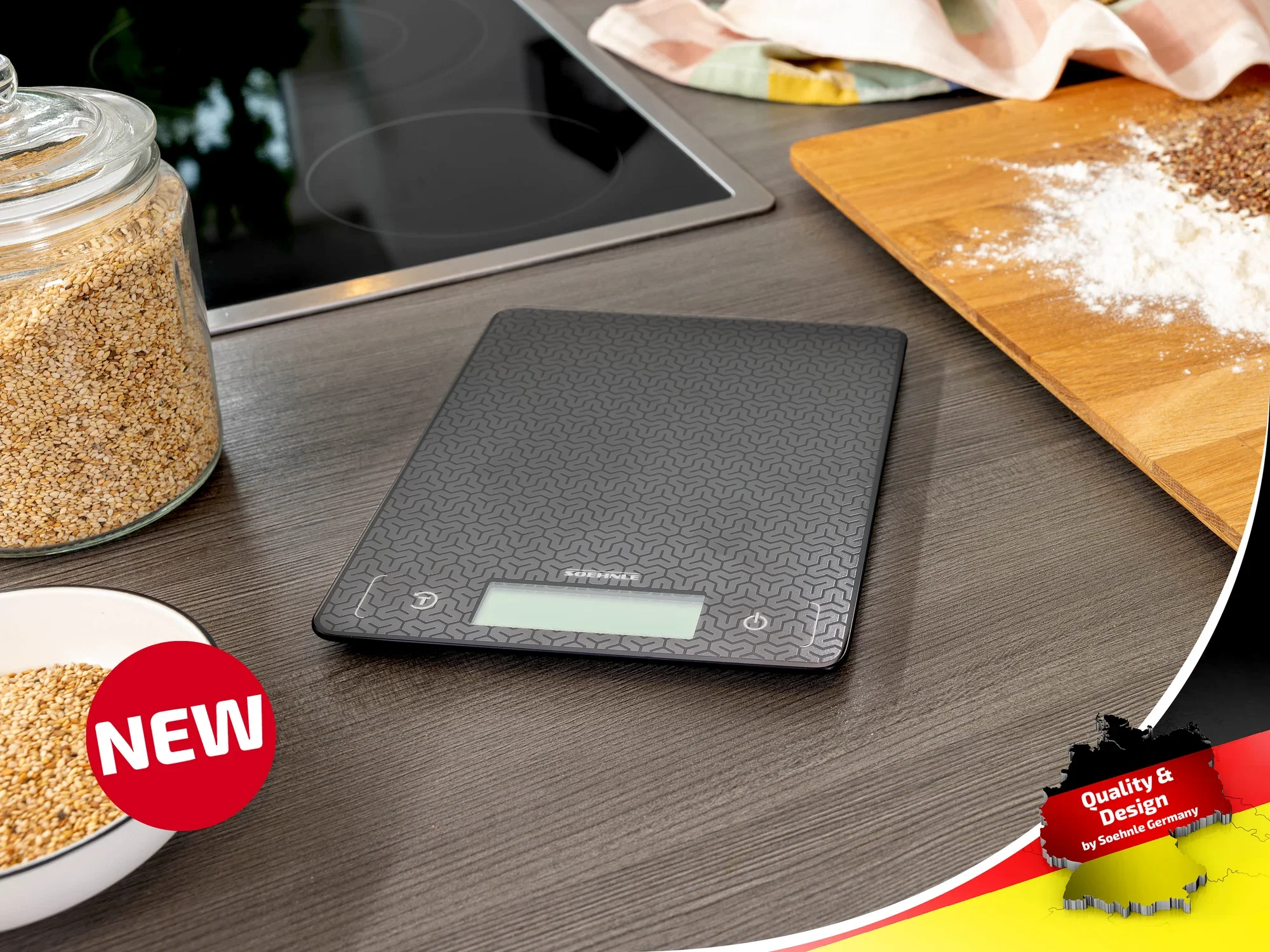 Cyfrowa waga kuchenna Soehnle na blacie roboczym, otoczona składnikami takimi jak mąka i płatki zbożowe. Waga ma nowoczesny design i czytelny wyświetlacz.