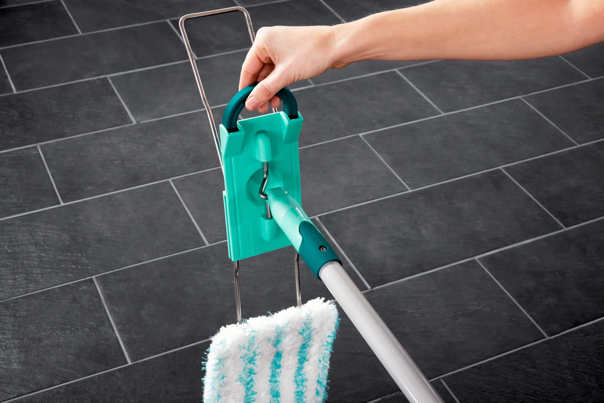 Un lavapavimenti Profi XL con manico in acciaio viene utilizzato su piastrelle scure. Una mano tiene l'impugnatura del lavapavimenti, dotato di una testa di pulizia verde.