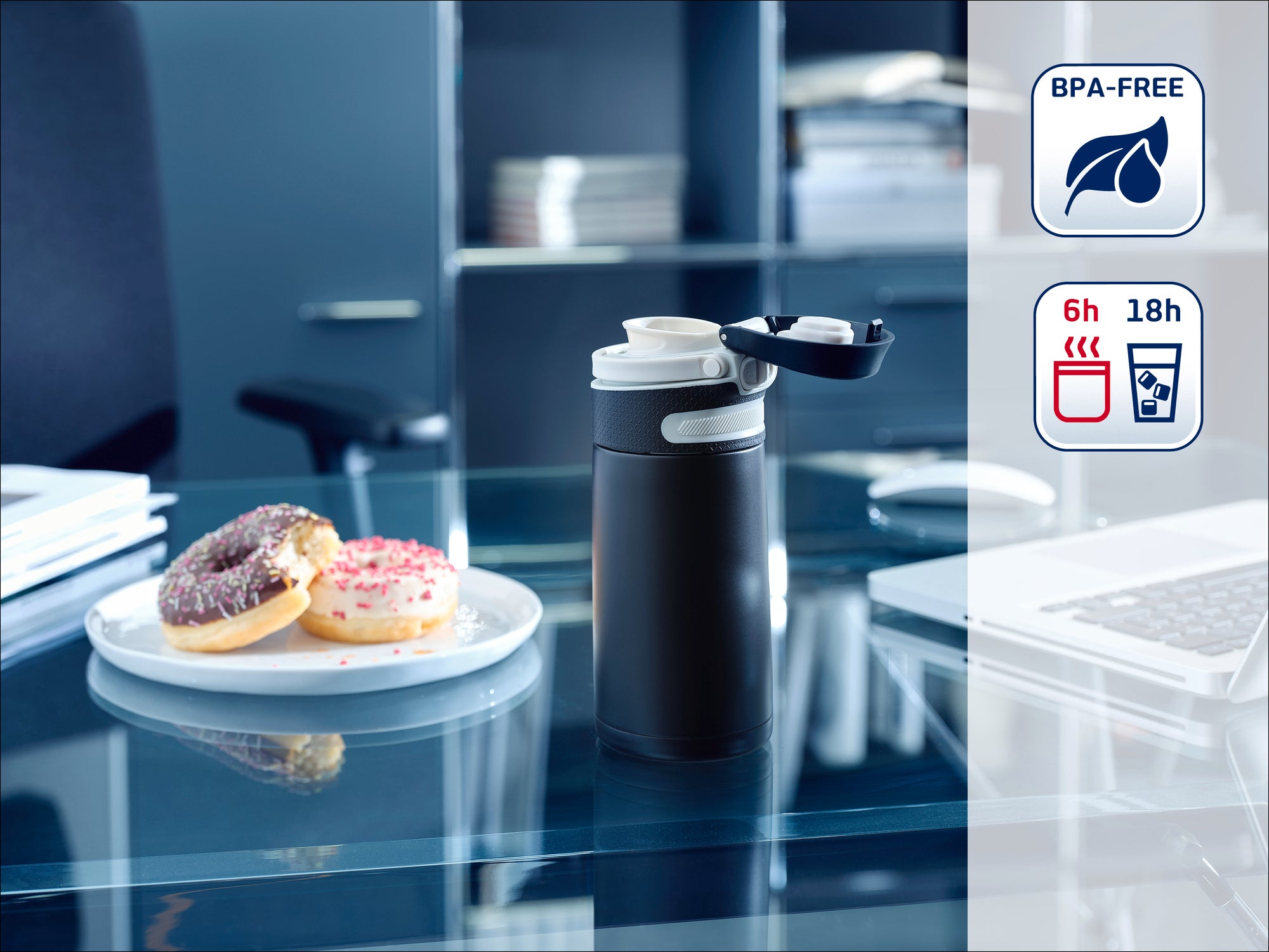 Thermobecher auf einem Schreibtisch mit geöffnetem Deckel, daneben ein Teller mit Donuts. Im Hintergrund sind Regale mit Büchern. BPA-frei, hält Getränke 6 Stunden heiß und 18 Stunden kalt.
