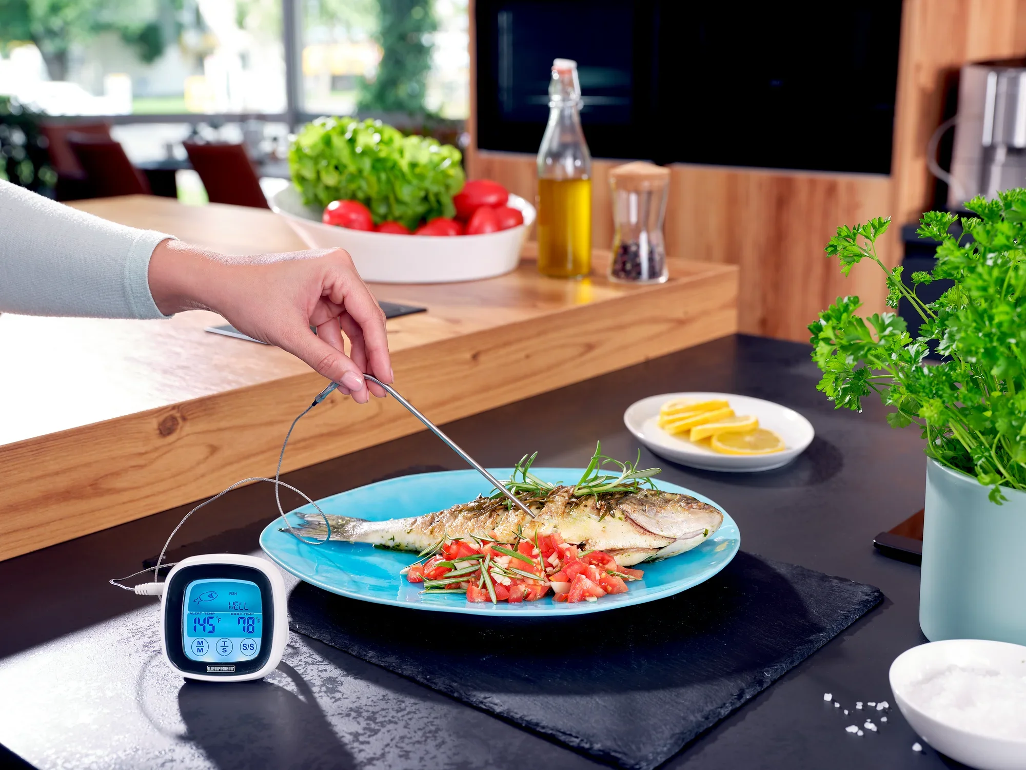Termometr do pieczeni i grilla służy do pomiaru temperatury pieczonej ryby na talerzu. W tle widoczne są świeże składniki, takie jak pomidory i zioła.