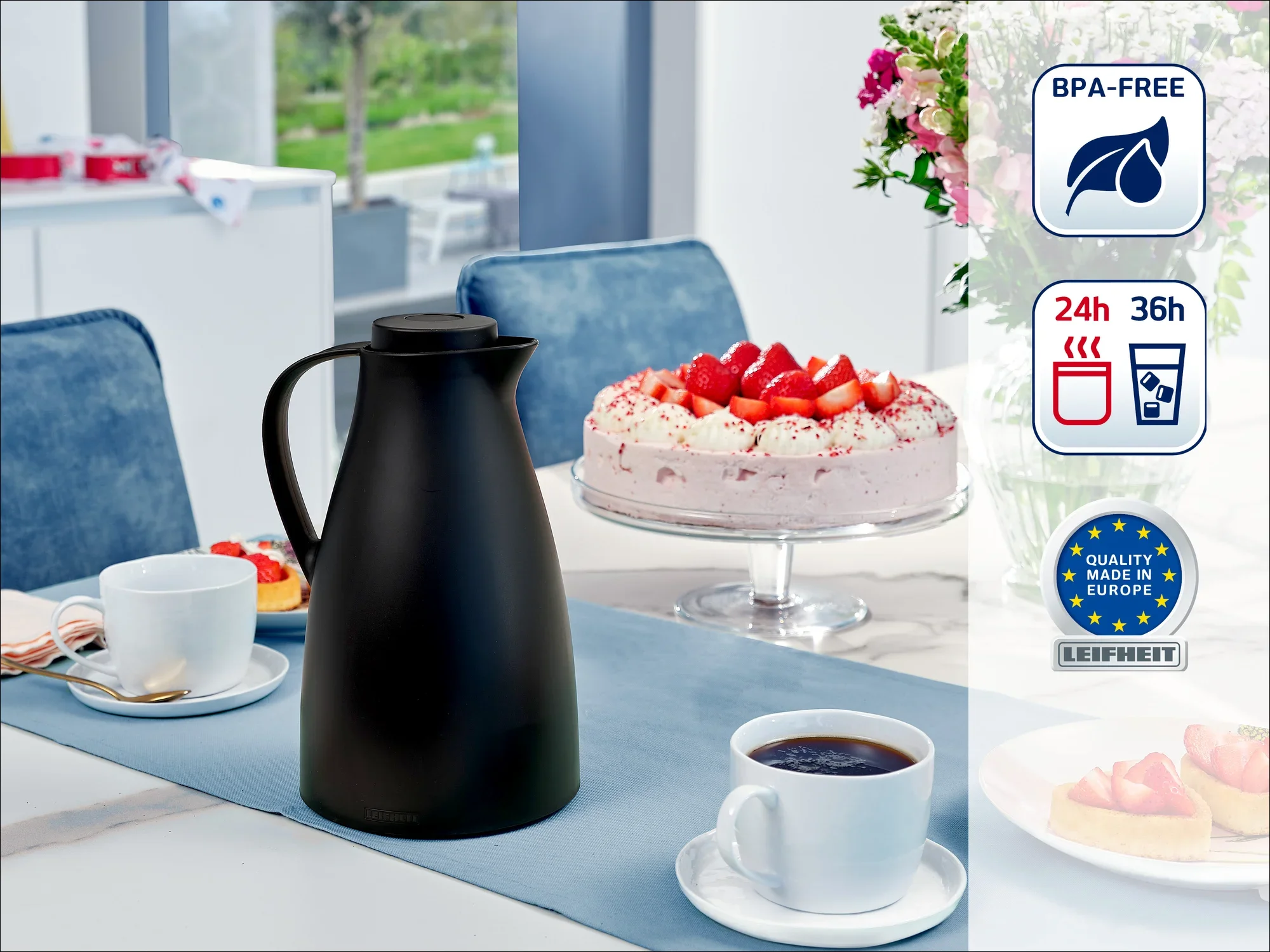 Una elegante jarra térmica negra sobre una mesa puesta con dos tazas de café y una tarta de fresas al fondo. La jarra no contiene BPA y mantiene las bebidas calientes entre 24 y 36 horas.