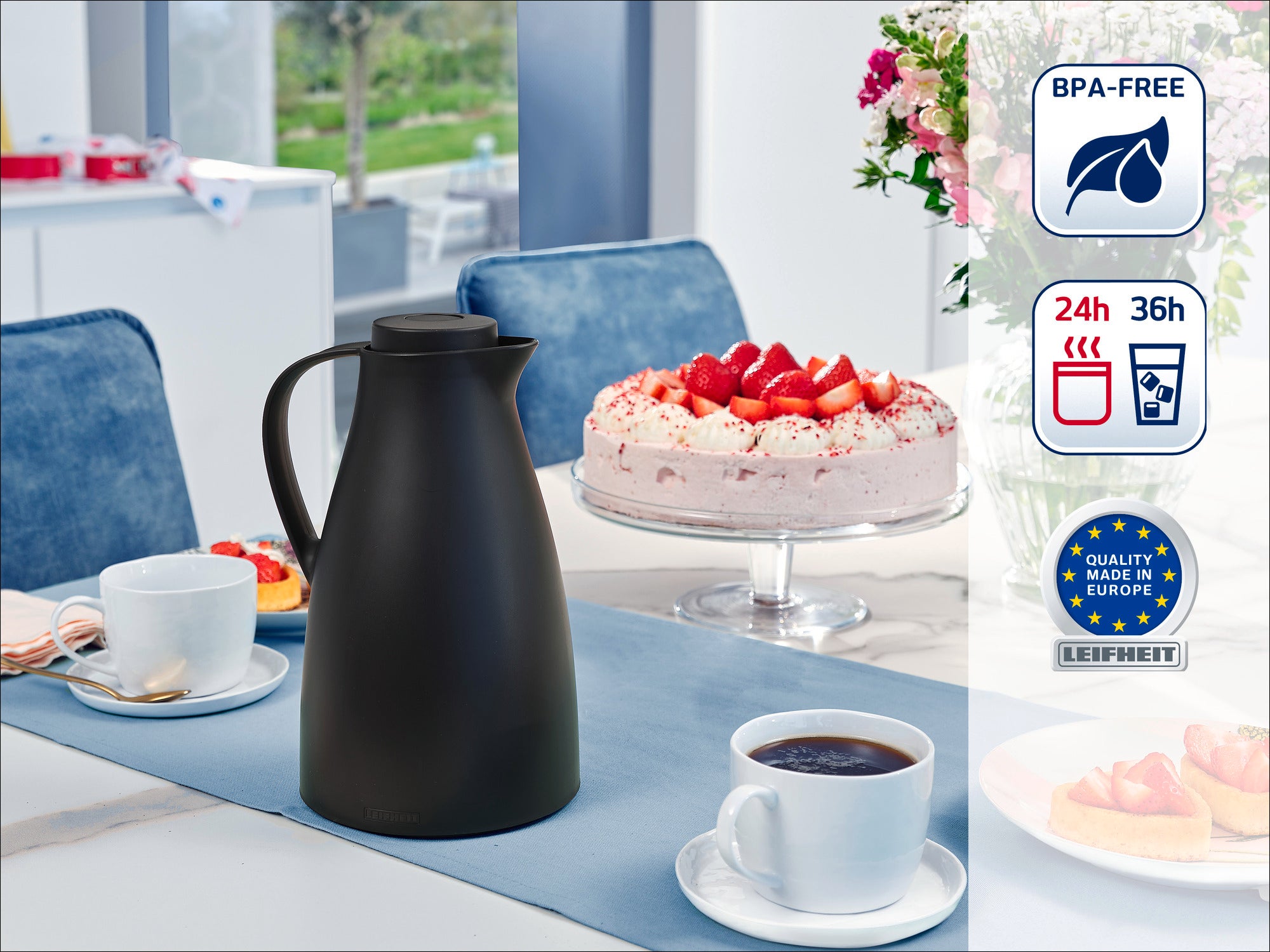 Een elegante zwarte thermoskan staat op een gedekte tafel met twee kopjes koffie en een aardbeientaart op de achtergrond. De kan is BPA-vrij en houdt dranken 24 tot 36 uur warm.