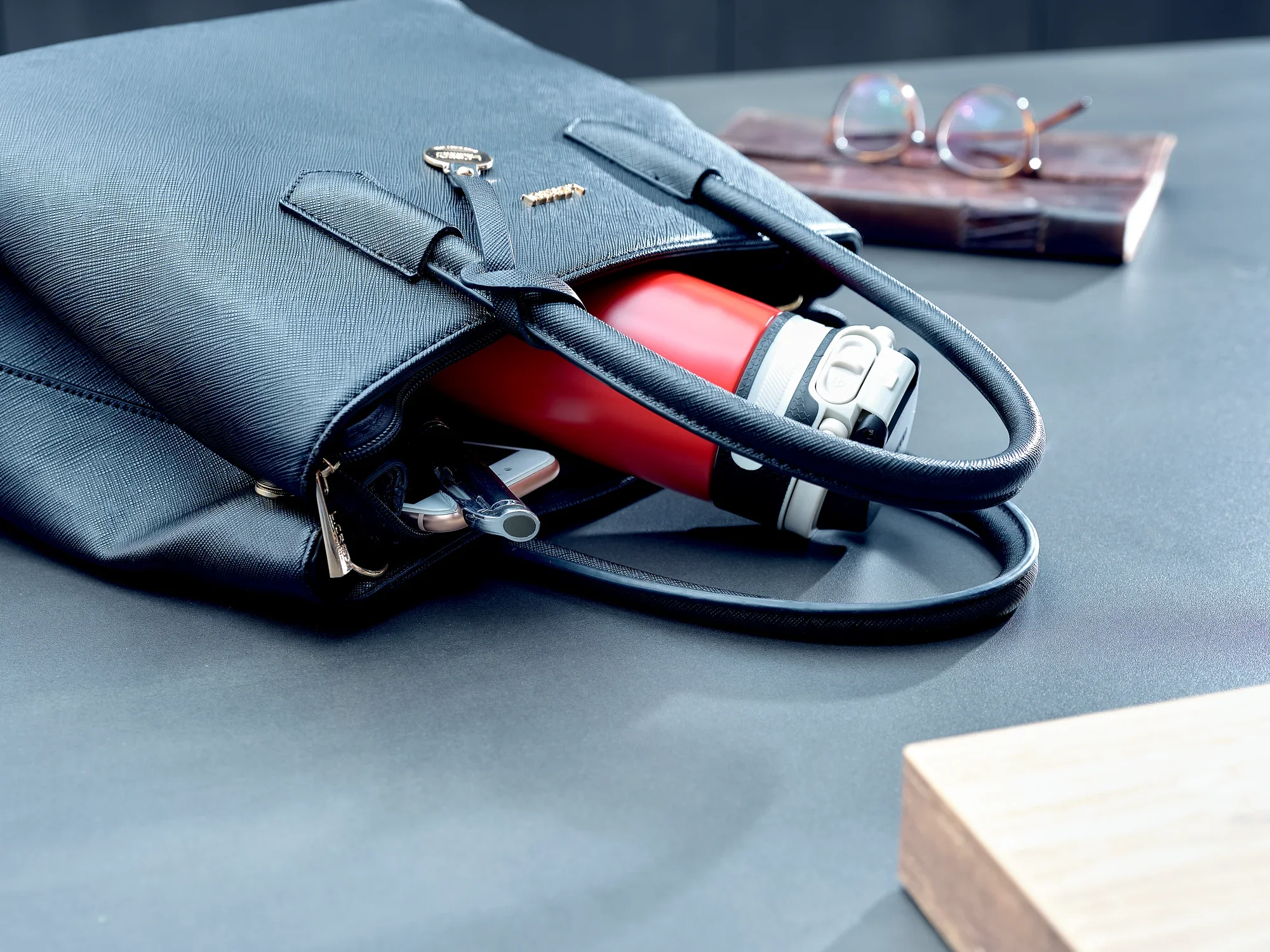 Izolowany kubek Flip 350 ml w kolorze czerwonym leży w otwartej czarnej torbie na stole. Obok torby znajduje się para szklanek i drewniany klocek. Idealny do podróży.