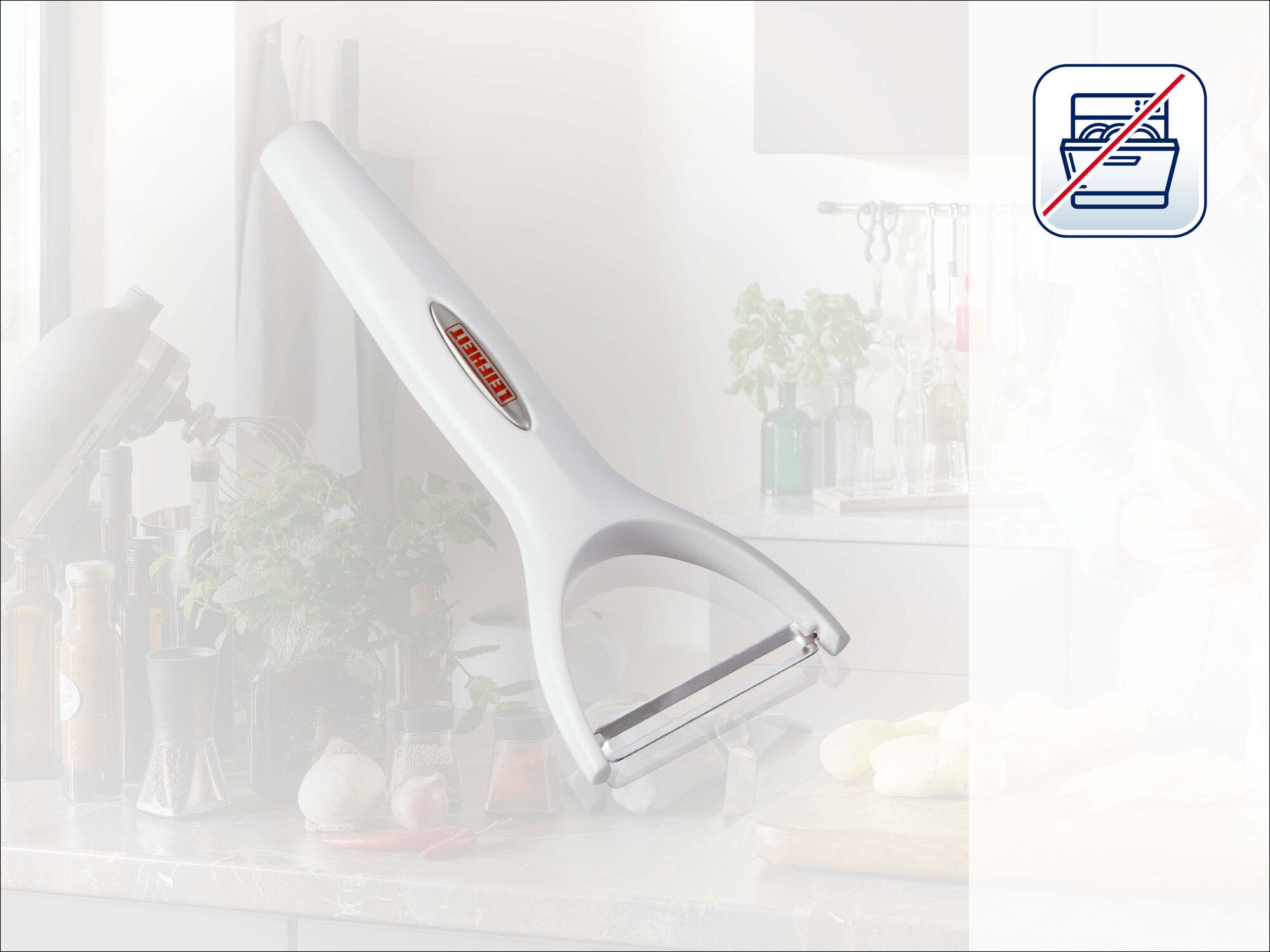 Leifheit Sparschäler 03151 in Weiß mit ergonomischem Griff und querliegender Klinge, schräg vor heller Küchenkulisse platziert; Symbol oben rechts weist auf spülmaschinengeeignete Reinigung hin.