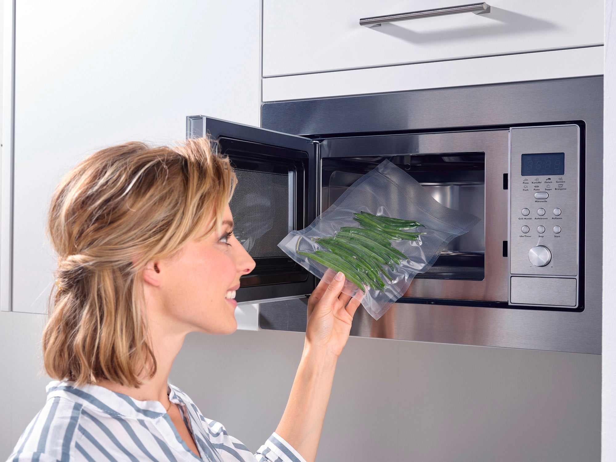 Een vrouw gebruikt een vacuümzak om sperziebonen op te warmen in de magnetron. De zak is doorzichtig en laat de verse bonen duidelijk zien. Ideaal om snel te koken.