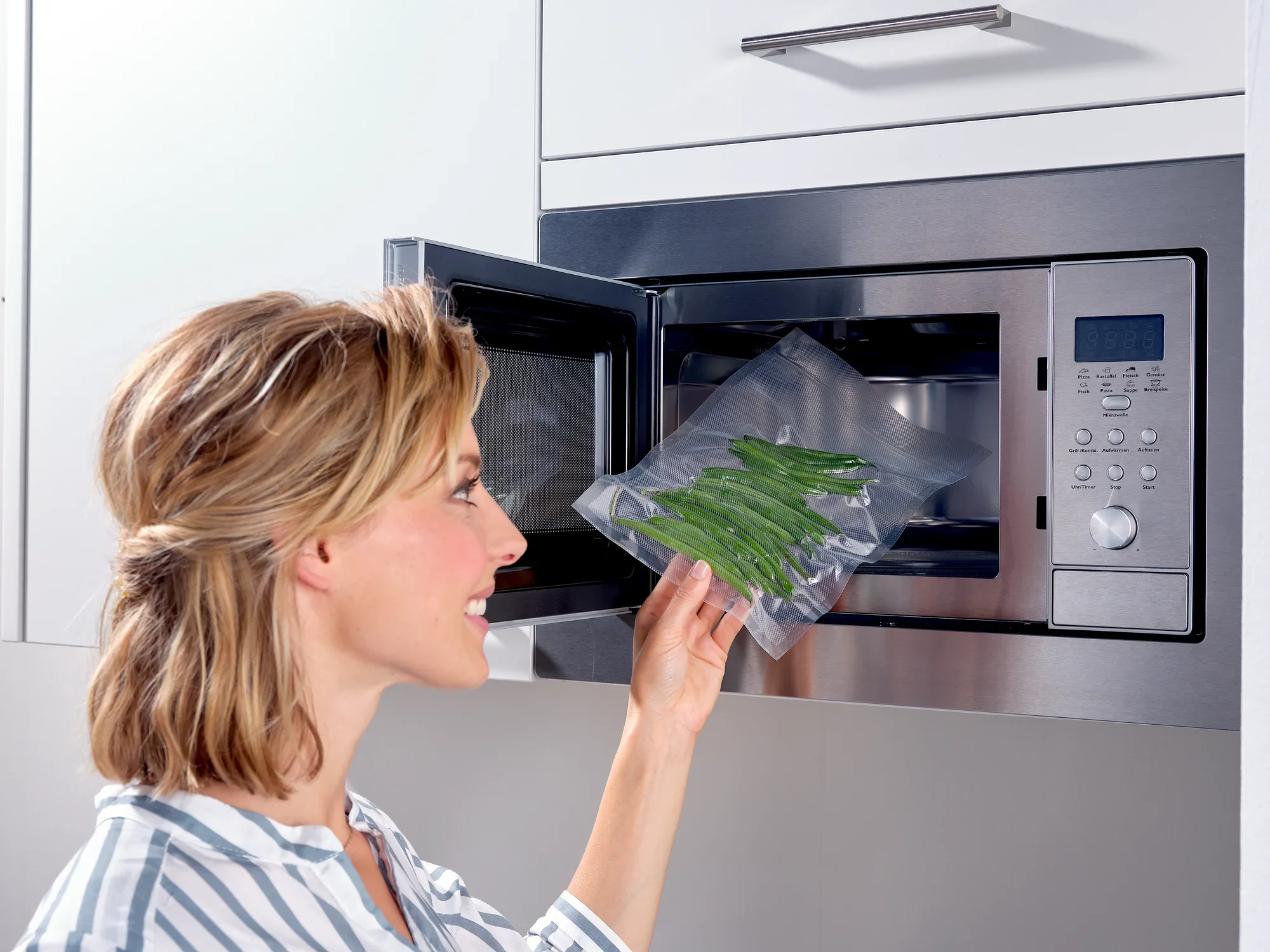 Una donna usa un sacchetto sottovuoto per riscaldare i fagiolini nel microonde. Il sacchetto è trasparente e mostra chiaramente i fagiolini freschi. Ideale per una cottura veloce.