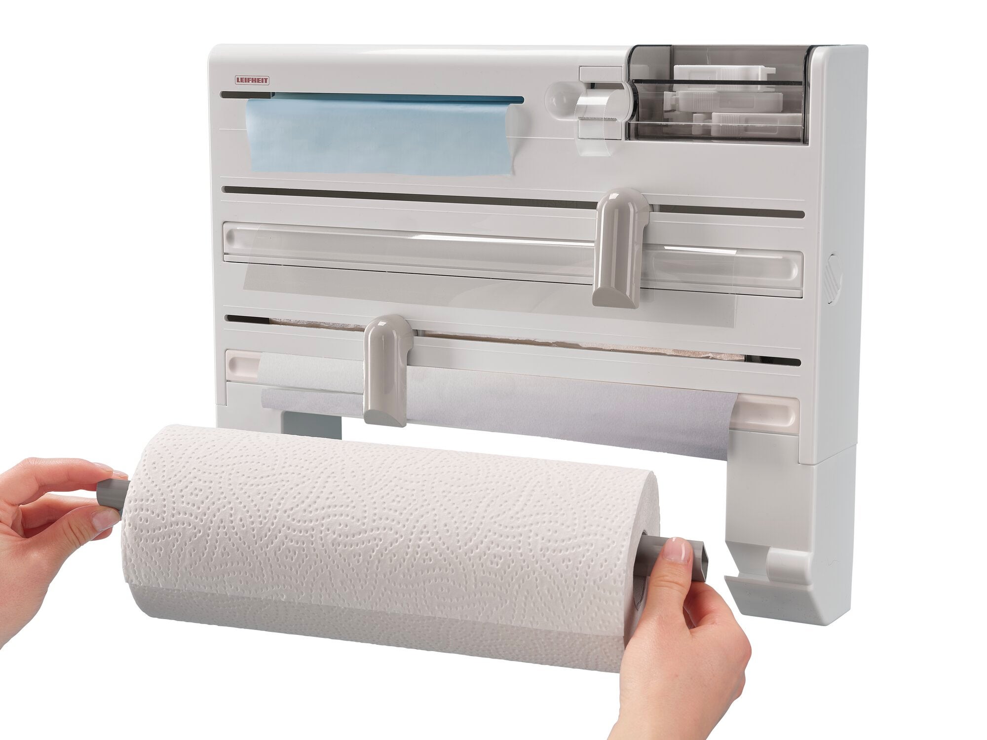 Support mural pour rouleaux Parat Plus : une personne installe un rouleau de papier essuie-tout dans le support mural blanc Parat Plus, qui offre de la place pour des films alimentaires et des torchons.