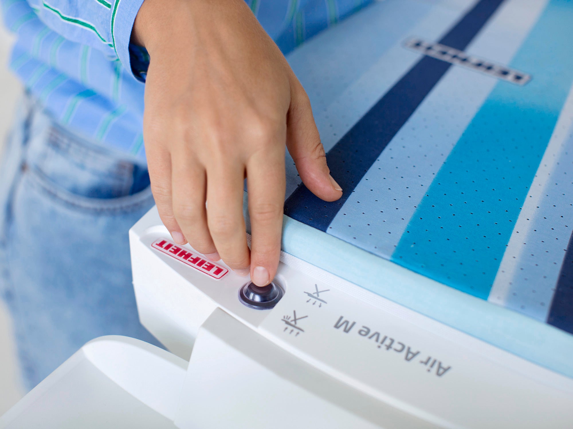 Bügelbrett Air Active Express M in Weiß. Eine Hand bedient den Knopf an der Seite des Bügelbretts. Das Brett hat ein modernes Design mit blauen Streifen.