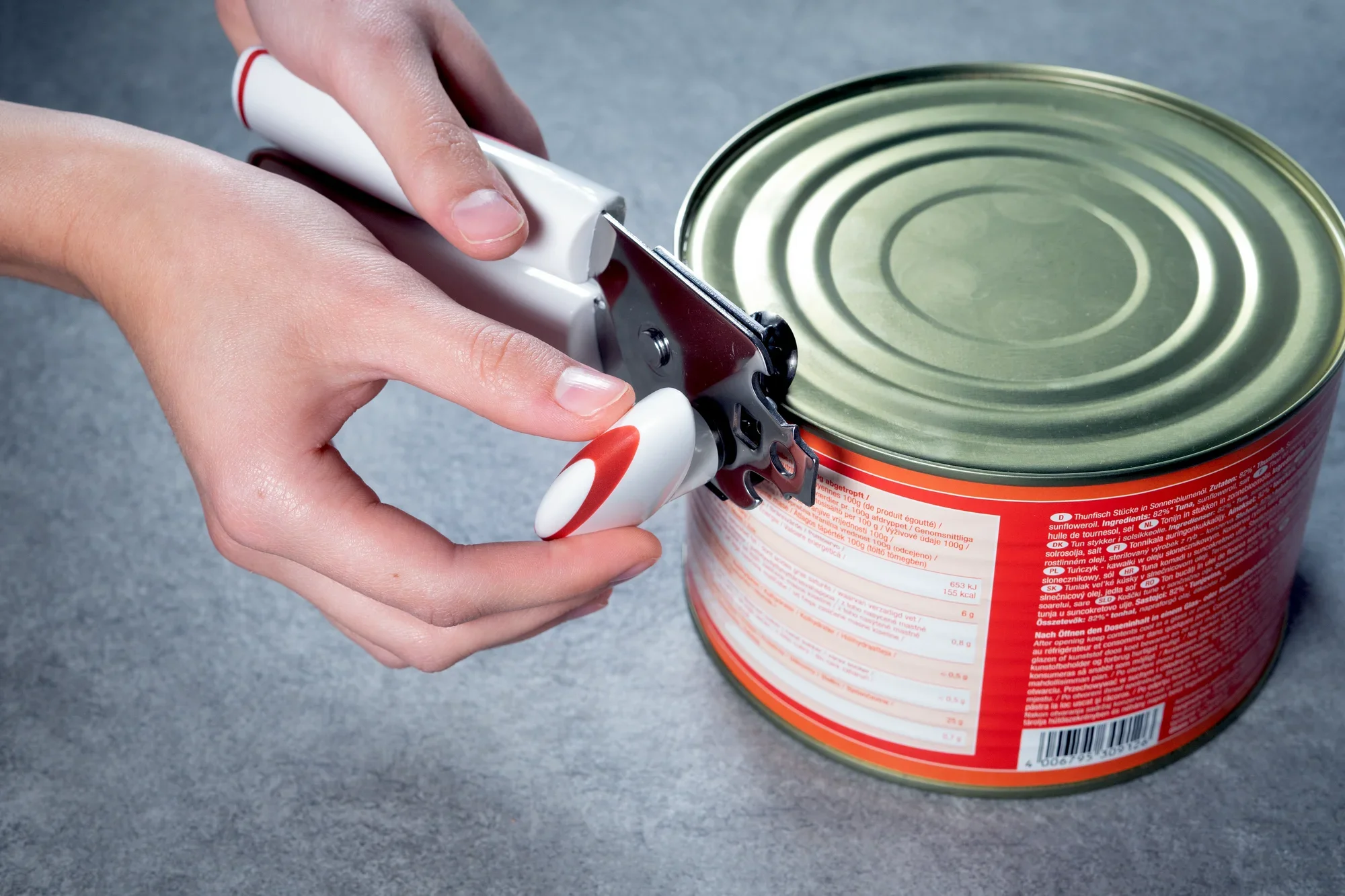 Dosenöffner Lifty in Anwendung: Eine Person benutzt den Dosenöffner Lifty, um eine Konservendose auf einem grauen Untergrund zu öffnen. Der ergonomische Griff erleichtert die Handhabung.
