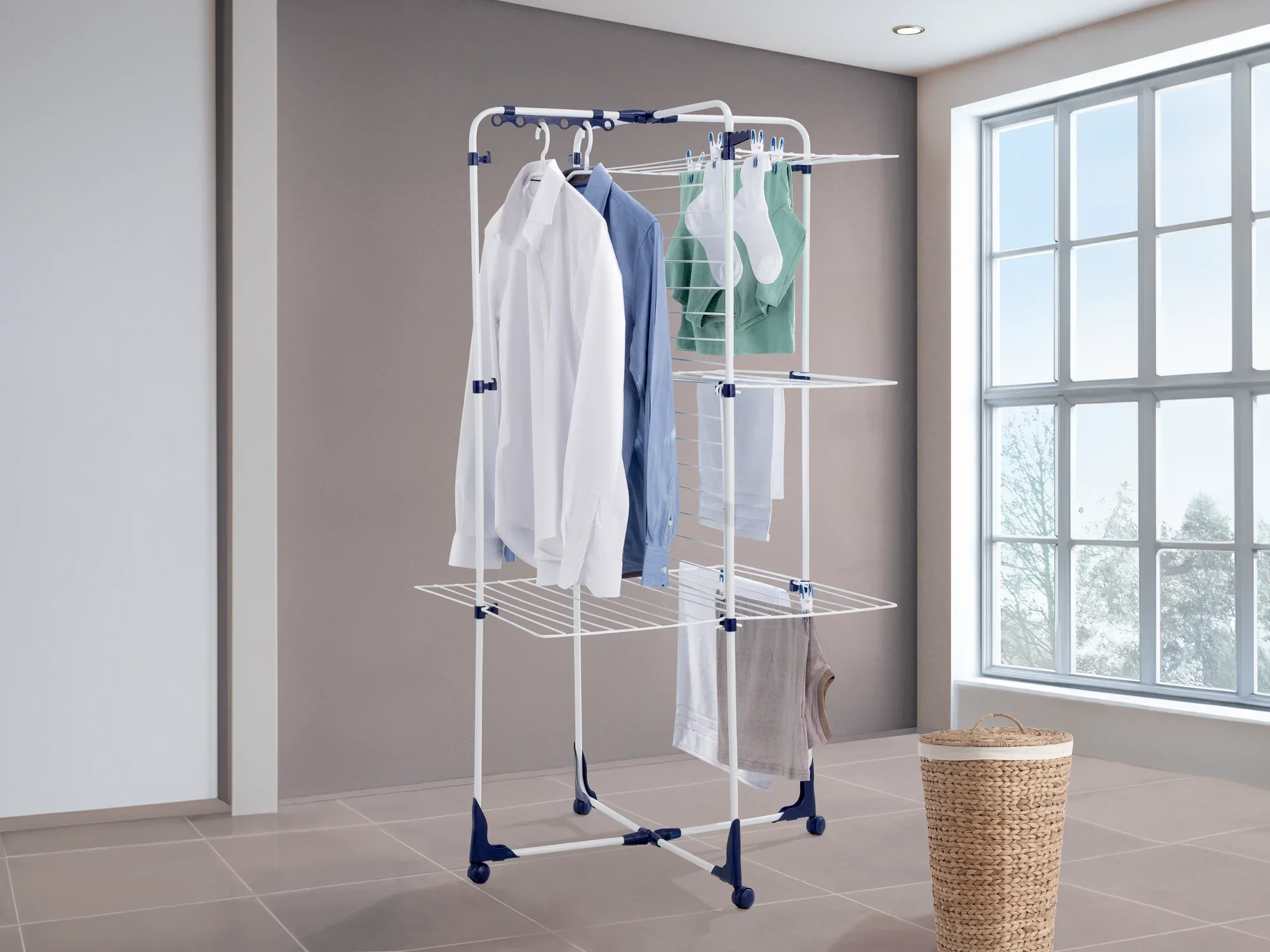 Classic Tower 340 torendroger: Een wit droogrek met meerdere niveaus en blauwe accenten staat in een lichte kamer. Het wordt opgehangen met overhemden, handdoeken en sokken.