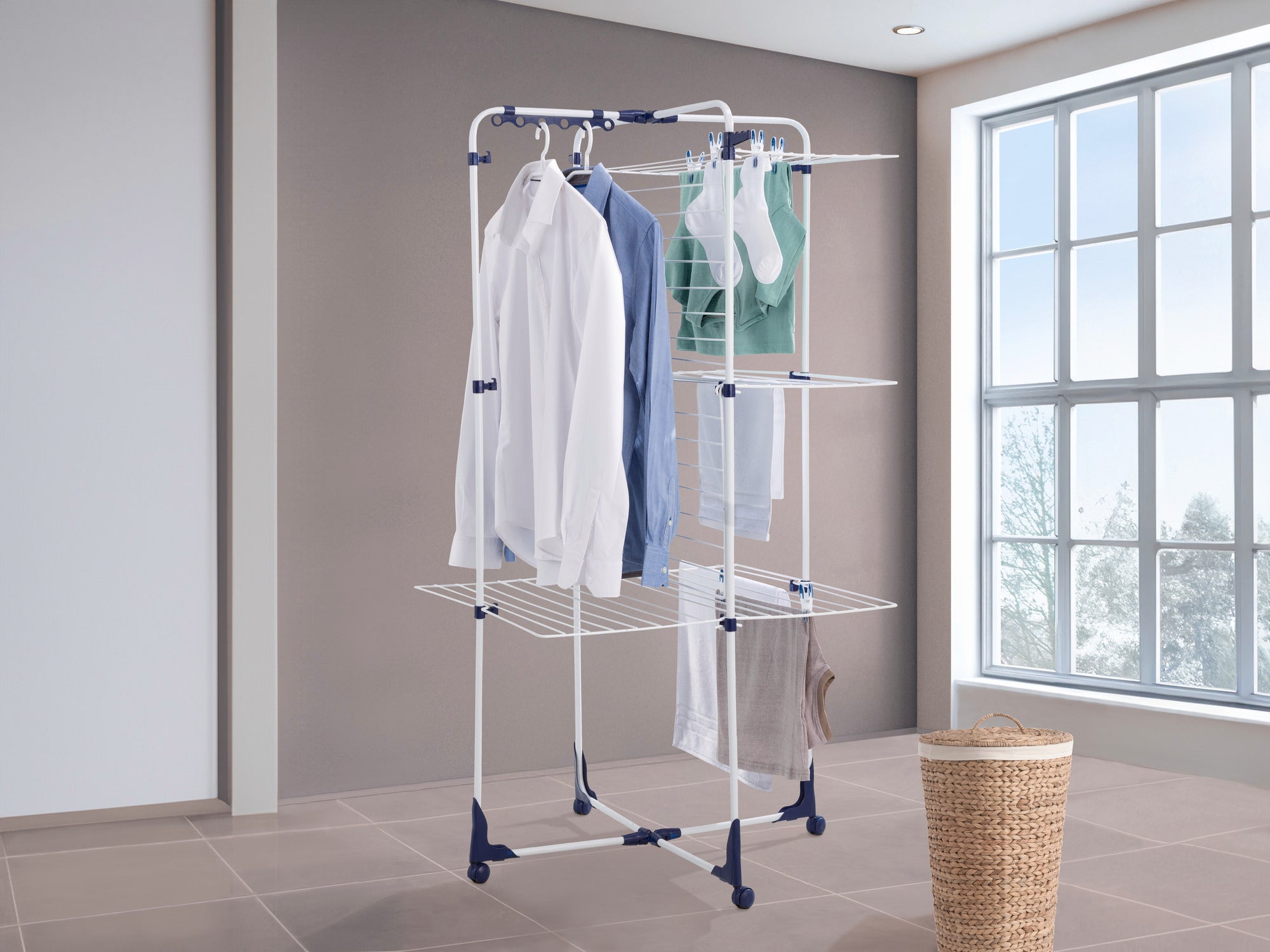 Classic Tower 340 torendroger: Een wit droogrek met meerdere niveaus en blauwe accenten staat in een lichte kamer. Het wordt opgehangen met overhemden, handdoeken en sokken.