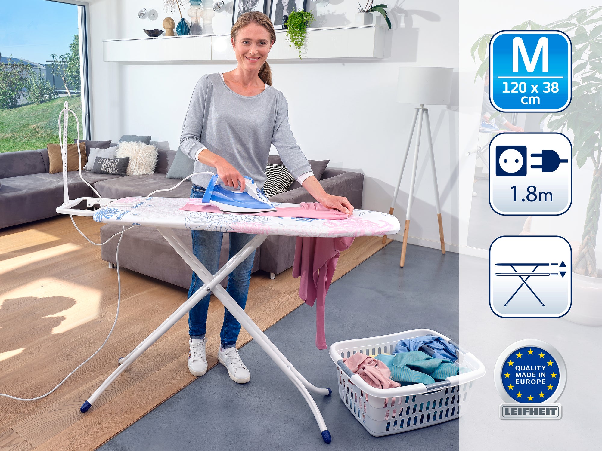 Eine Frau bügelt auf einem mittelgroßen Bügeltisch in einem hellen Wohnzimmer. Der Tisch hat eine Fläche von 120 x 38 cm und eine Kabellänge von 1,8 m. Qualität Made in Europe.