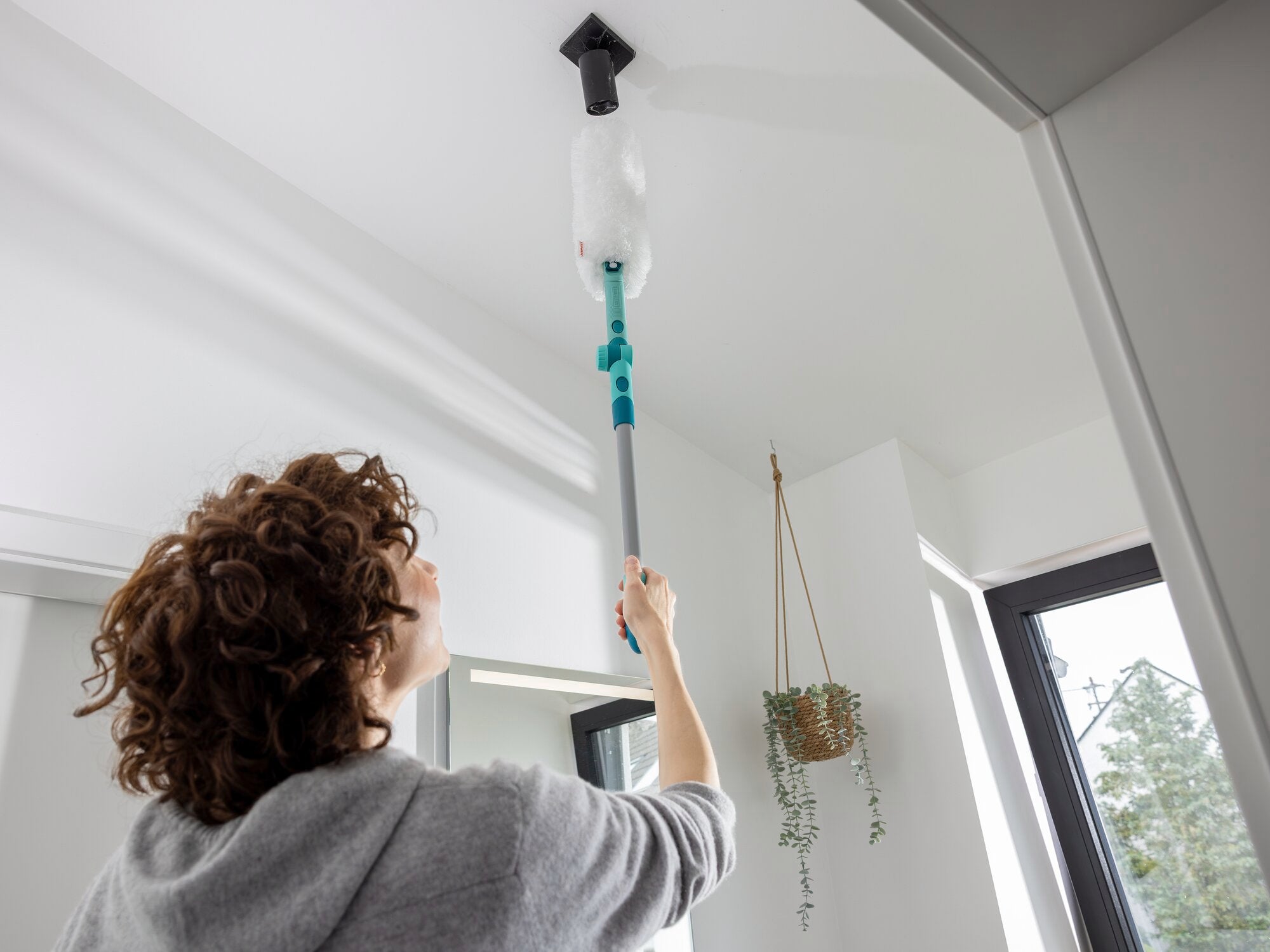 Eine Person verwendet den SUPERDUSTER XL Pro Reach, um eine hohe Decke zu reinigen. Der Staubwedel erreicht mühelos schwer zugängliche Stellen und sorgt für Sauberkeit.