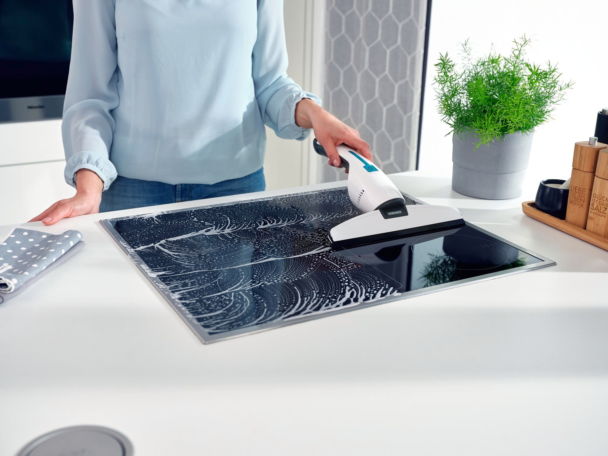 A person is cleaning a smooth surface with the Nemo window vacuum cleaner. The vacuum cleaner effectively removes water and dirt, while a plant in the background creates a fresh atmosphere.