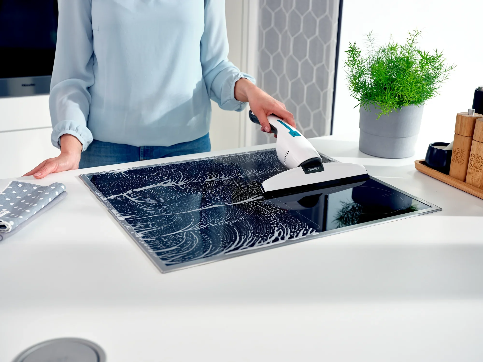 Eine Person reinigt eine glatte Oberfläche mit dem Nemo Fenstersauger. Der Sauger entfernt effektiv Wasser und Schmutz, während eine Pflanze im Hintergrund für eine frische Atmosphäre sorgt.