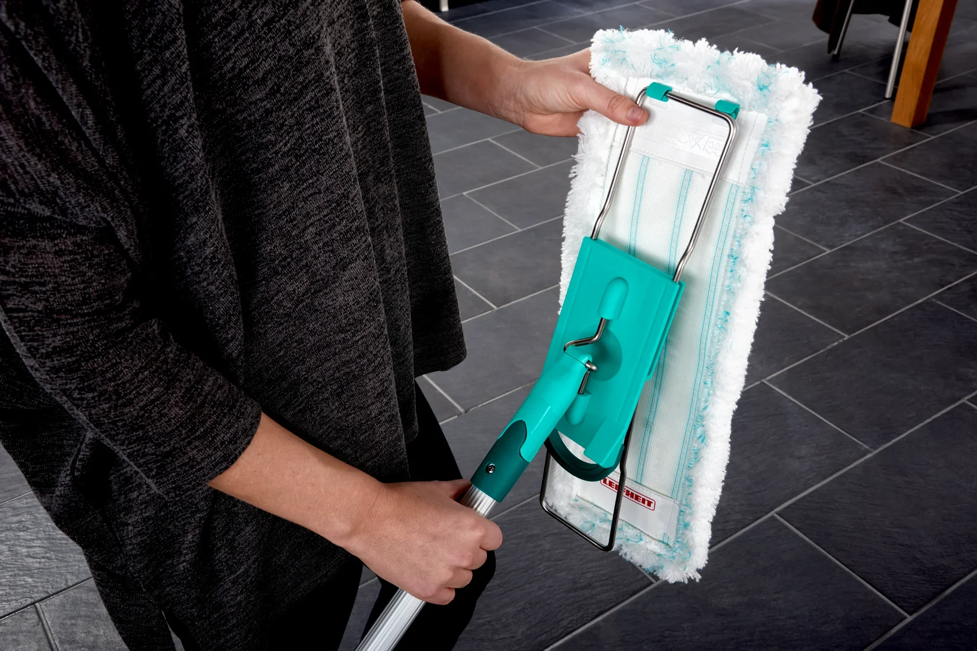 Een persoon gebruikt de Profi XL vloermop met een blauwe steel en een witte microvezeldoek op een donkere tegelvloer. De mop is ideaal voor een grondige reiniging en eenvoudig gebruik.