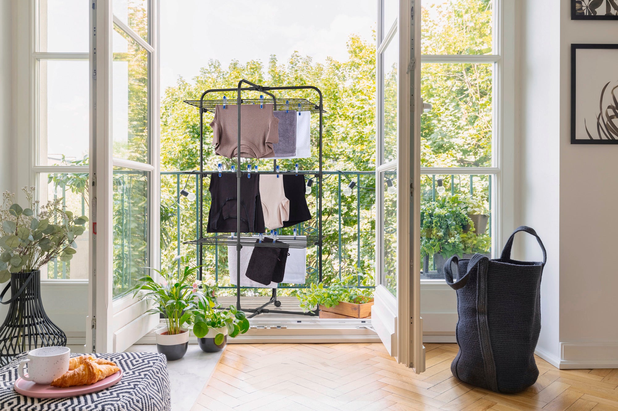 Classic Tower 270 Black tower dryer on a balcony with a view of the countryside. The dryer is hung with clothes, surrounded by plants and a laundry basket.