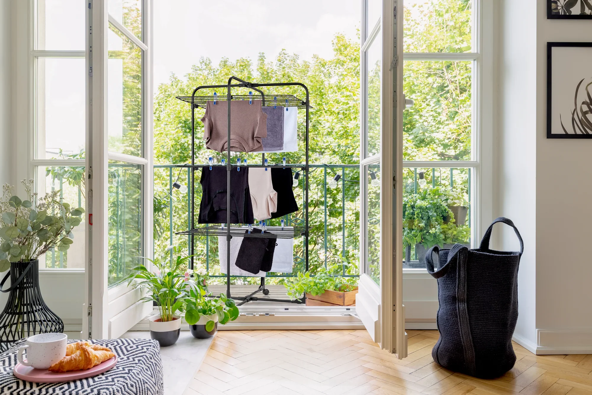 Classic Tower 270 Black tower dryer on a balcony with a view of the countryside. The dryer is hung with clothes, surrounded by plants and a laundry basket.