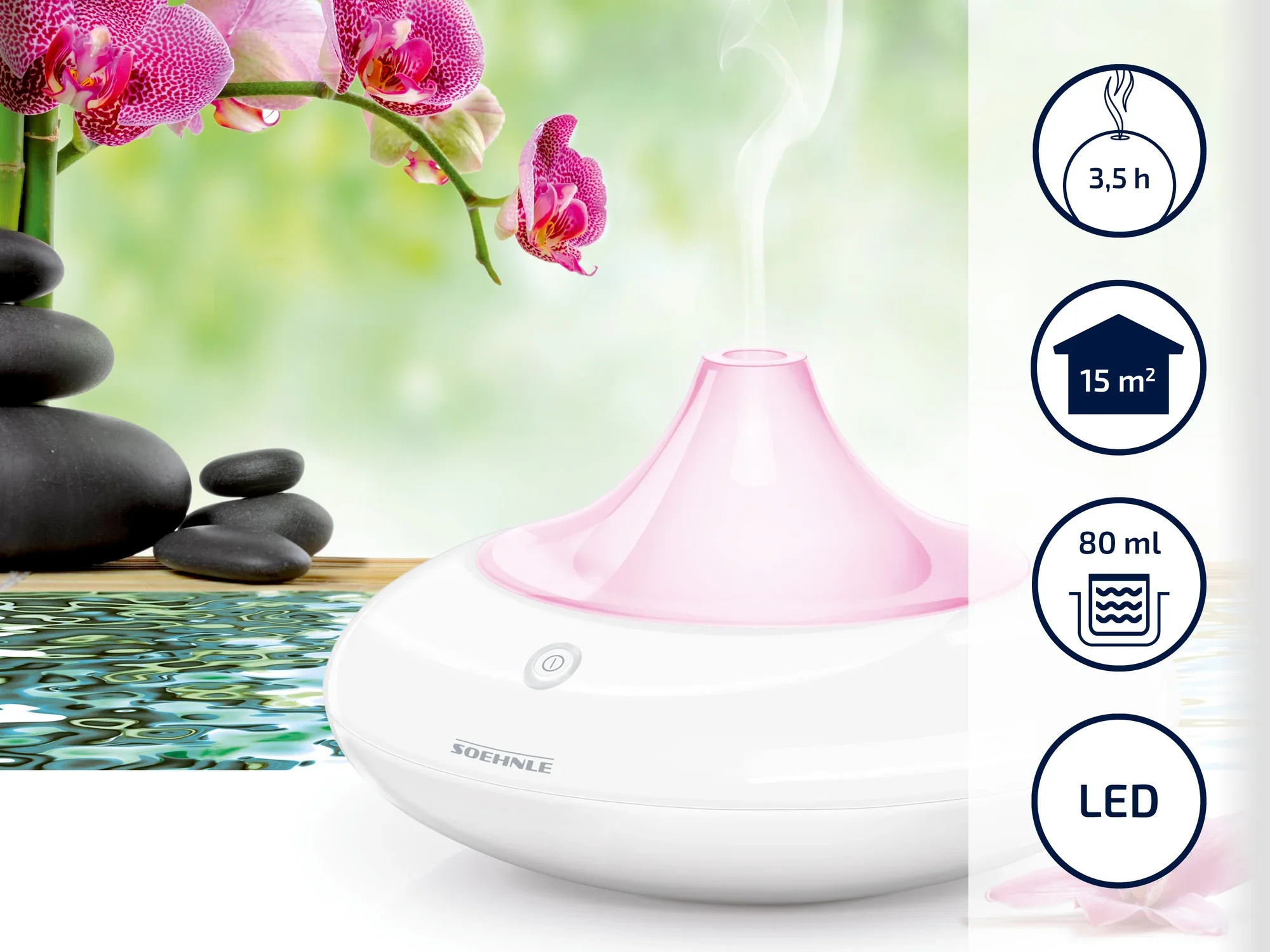 Un humidificateur rond et blanc avec des accents roses de Soehnle est placé à côté d'un jardin zen et d'orchidées. Il a une autonomie de 3,5 heures, convient pour 15 m², a une capacité de 80 ml et dispose d'un éclairage LED.