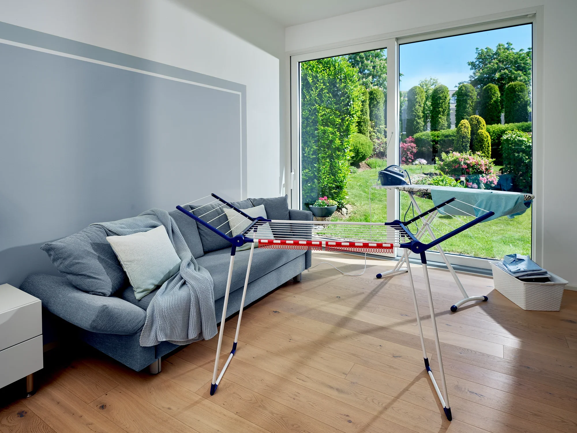 Wolnostojąca suszarka bębnowa Pegasus 150 Solid Slim stoi w nowoczesnym salonie z widokiem na zadbany ogród. Suszarka jest kompaktowa i idealna do małych przestrzeni.