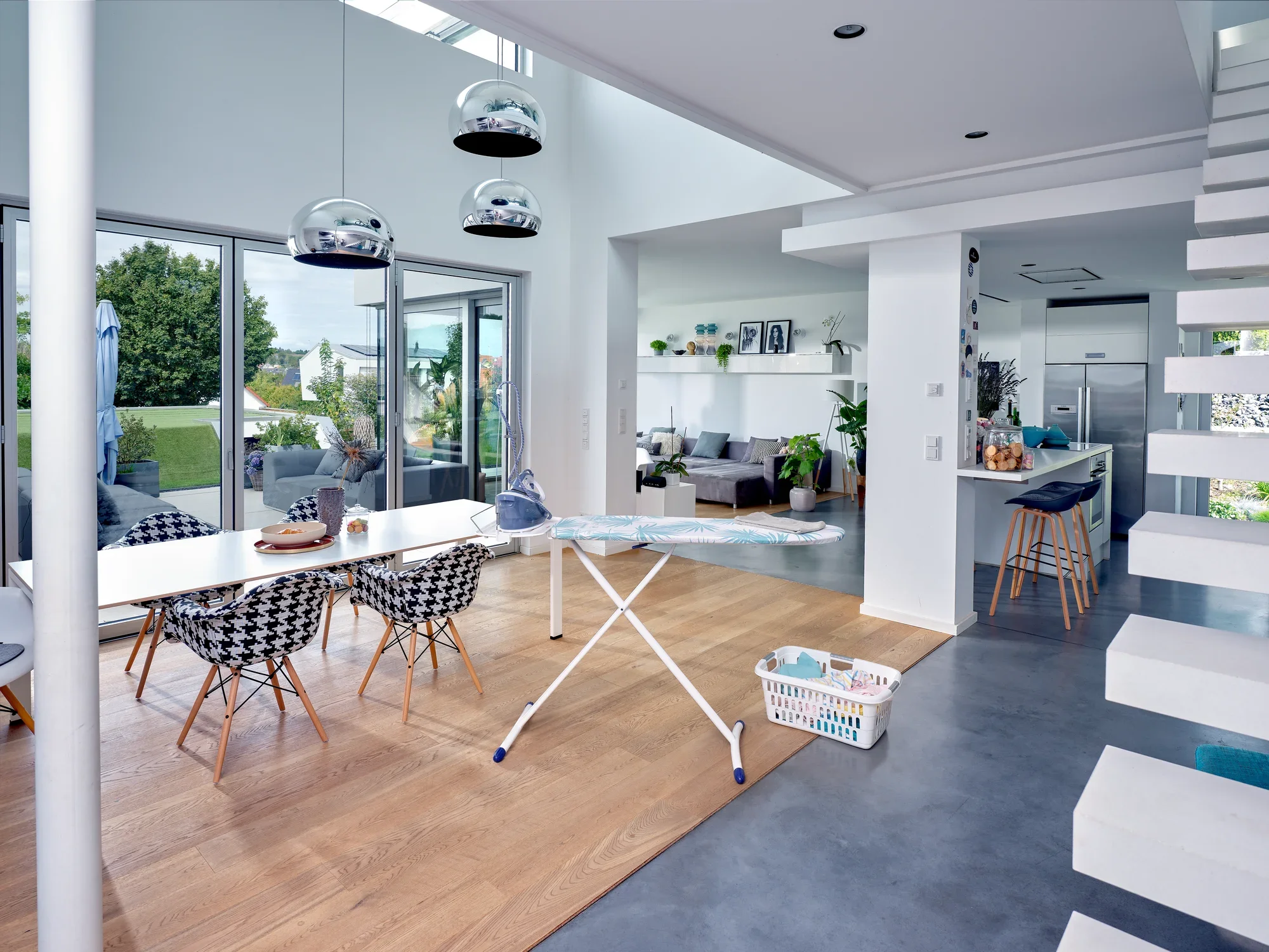 Table à repasser Air Board Express M Solid dans un salon moderne et lumineux. La table se trouve à côté d'une table avec des chaises et un panier à linge.