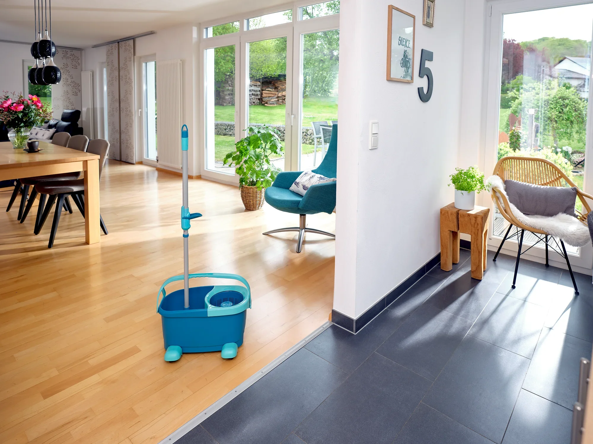 Een CLEAN TWIST Disc Mop Ergo Set staat in een moderne, lichte woonkamer met houten vloeren. Grote ramen laten veel licht binnen en planten creëren een gezellige sfeer.