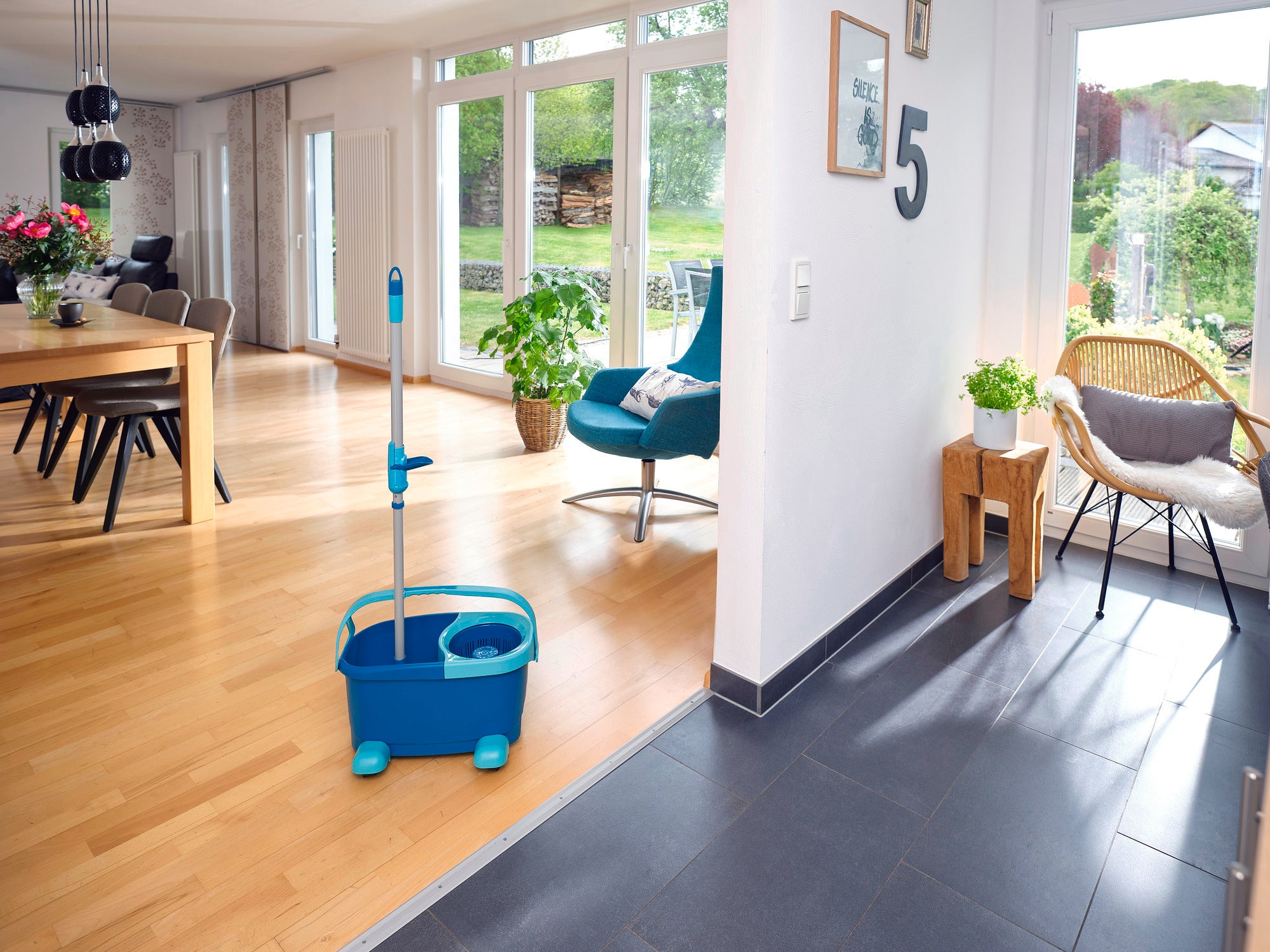 Un kit CLEAN TWIST Disc Mop Ergo se trouve dans un salon moderne et lumineux avec un sol en bois. De grandes fenêtres laissent entrer beaucoup de lumière et des plantes créent une atmosphère chaleureuse.